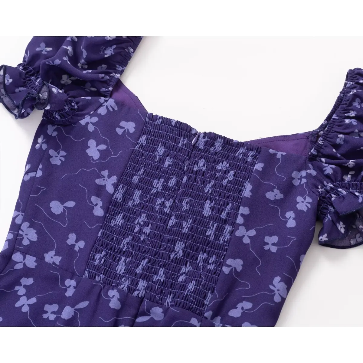 Close-up of the back of a purple floral print dress, showing the smocked panel, hidden zipper, and puff sleeve construction.