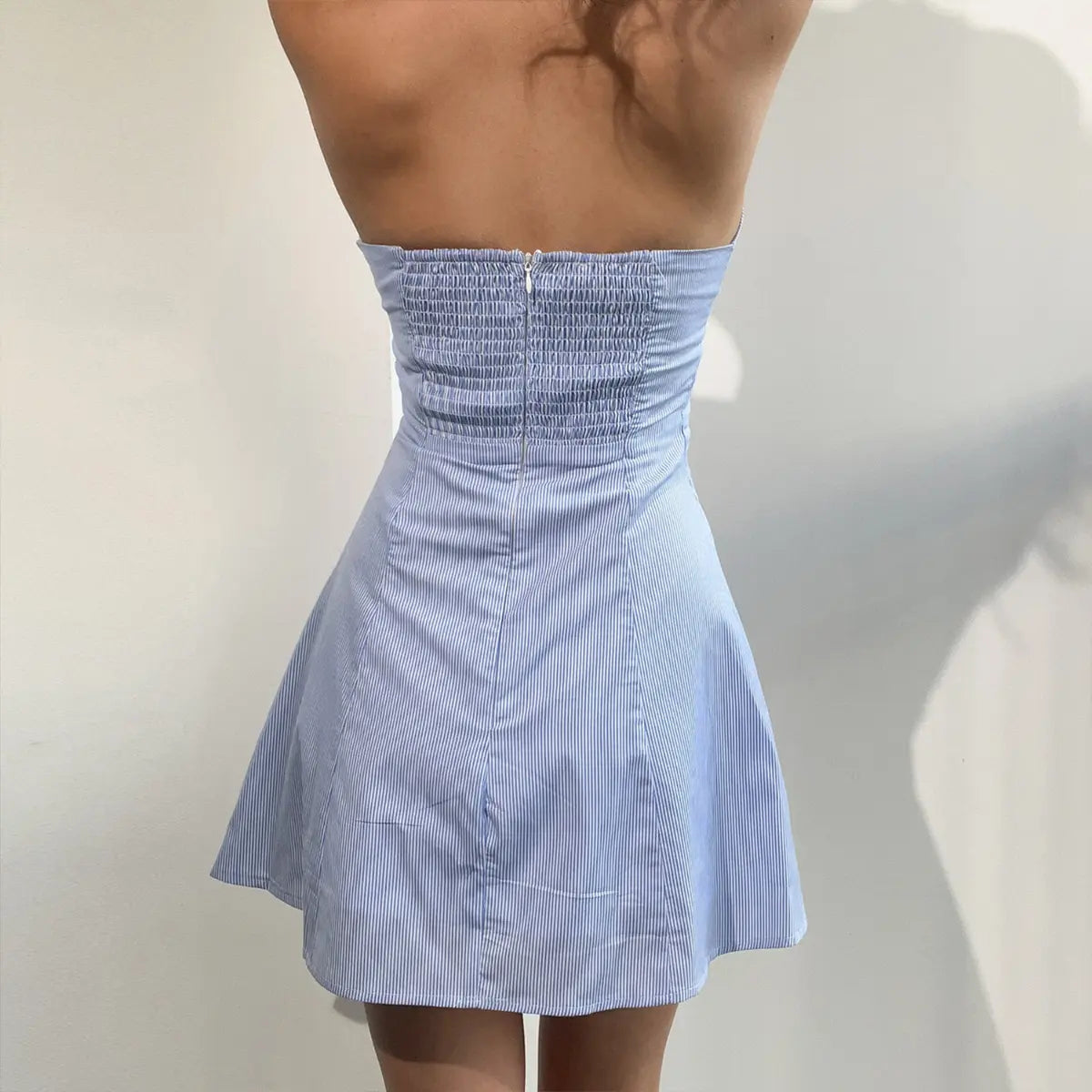 Back view of a blue and white striped halter mini dress, showing the smocked back panel and hidden zipper closure.