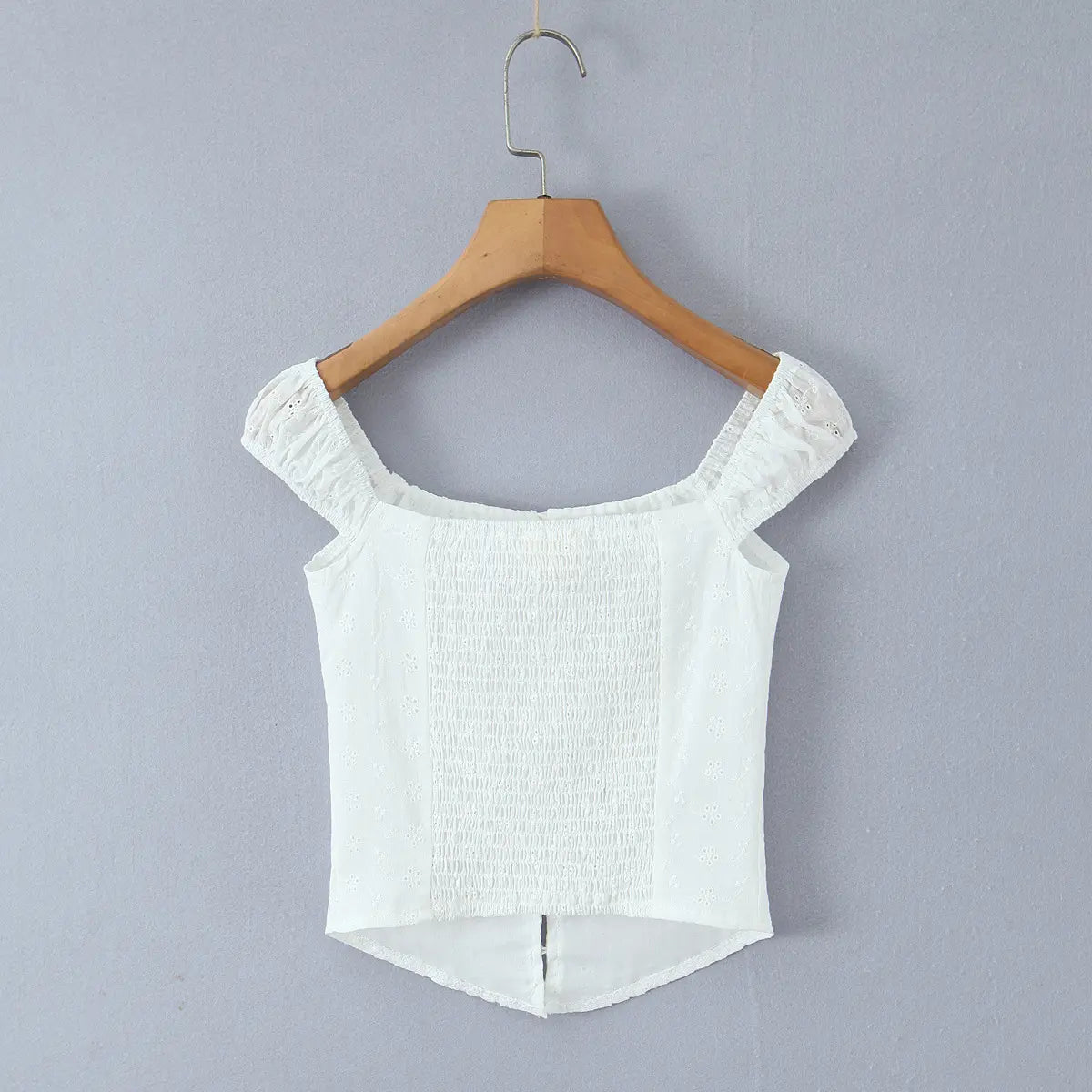 Full back view of a white eyelet embroidered bustier top on a hanger, showcasing the wide smocked elastic panel.