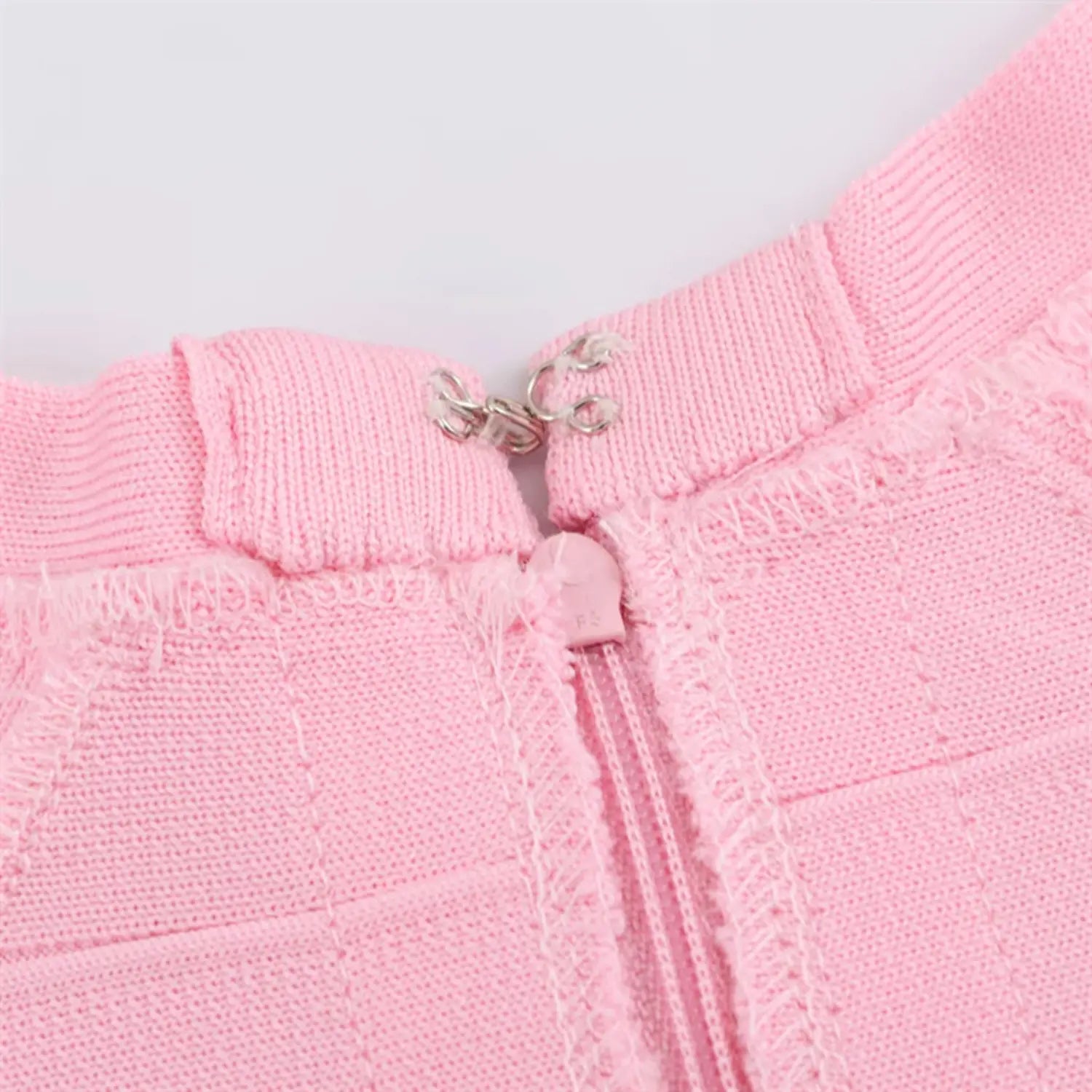 Extreme macro shot of zipper top, silver metal hook & eye fastener, frayed knit seam binding, matching pink zipper tape