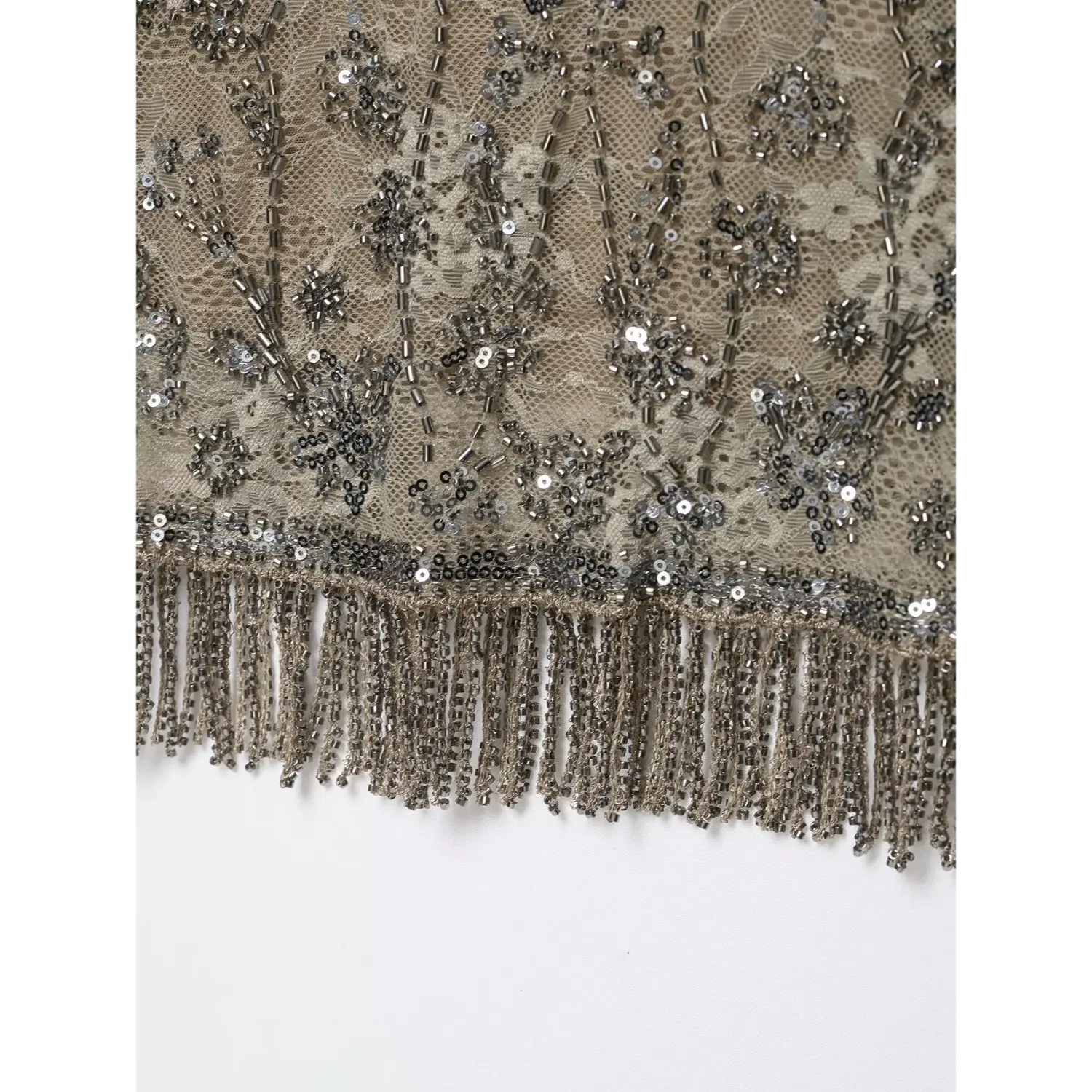 Close‑up bottom hem view showing hanging beaded fringe and sequin border trim on beige lace top