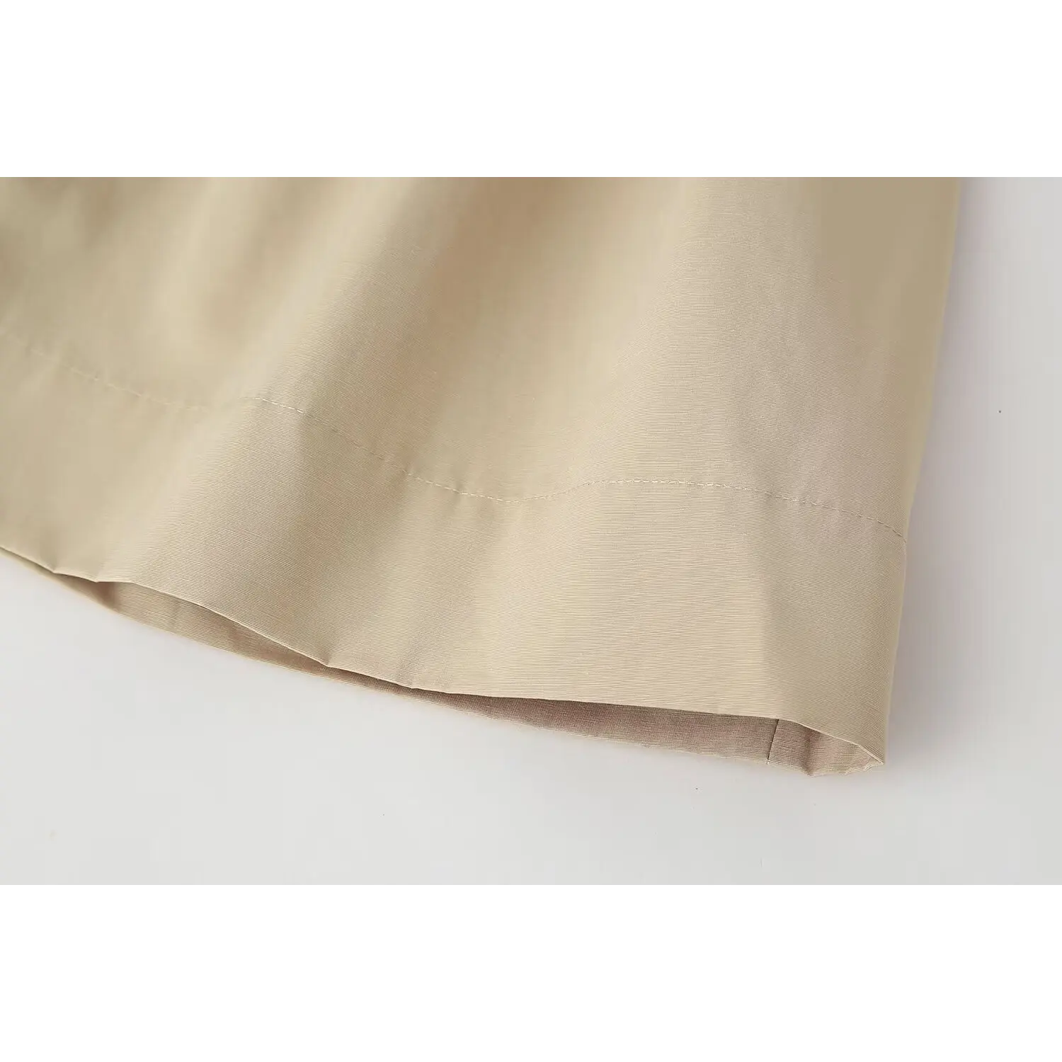 Close‑up view of hem stitching detail on beige belted mini dress, smooth lightweight fabric, neat finished seam, white background