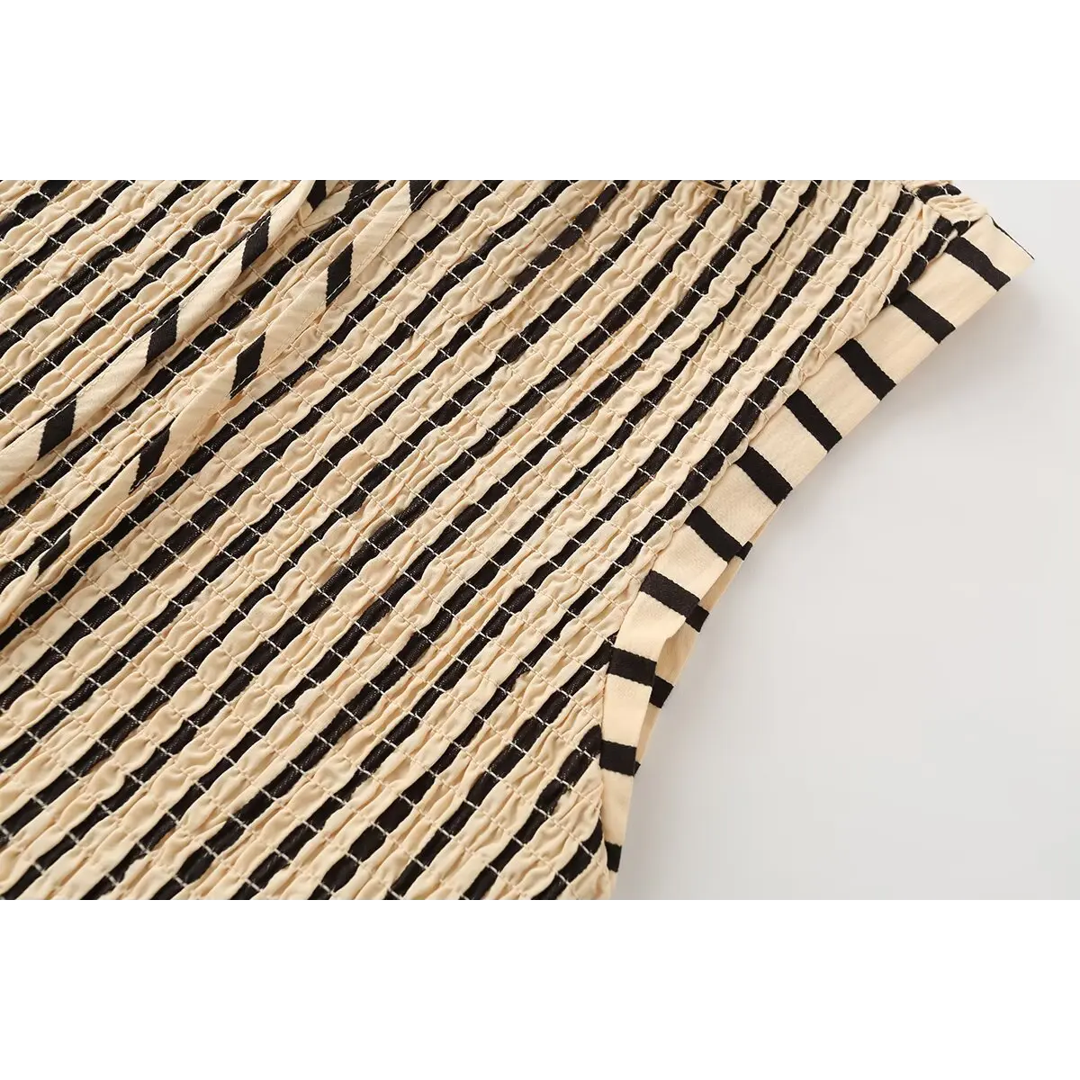 Close-up of the top's smocked texture, showing the beige and black stripes and cap sleeve.