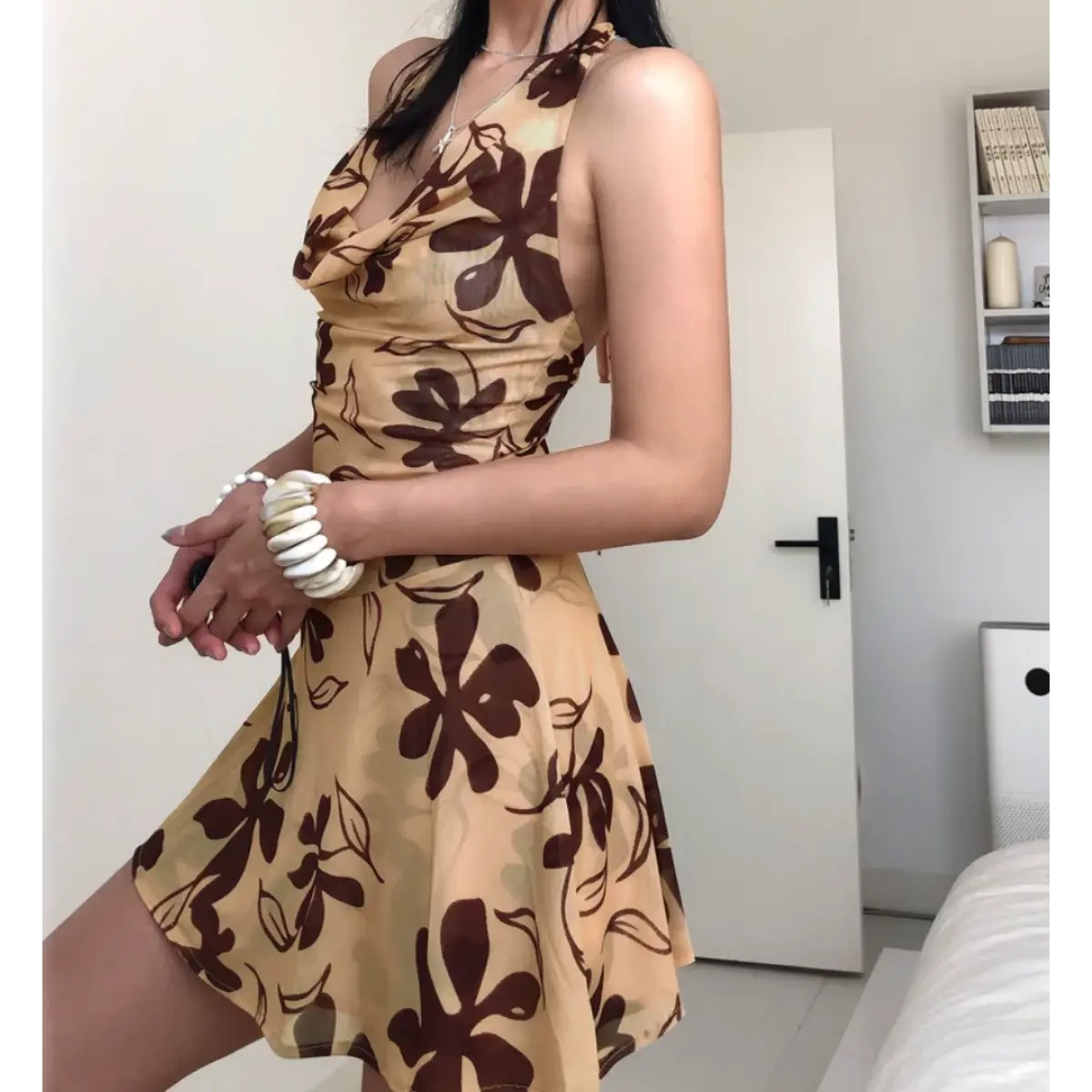 Woman wearing a beige halter mini dress with a brown floral print, posed with crossed arms to highlight the fitted bodice and flared skirt.