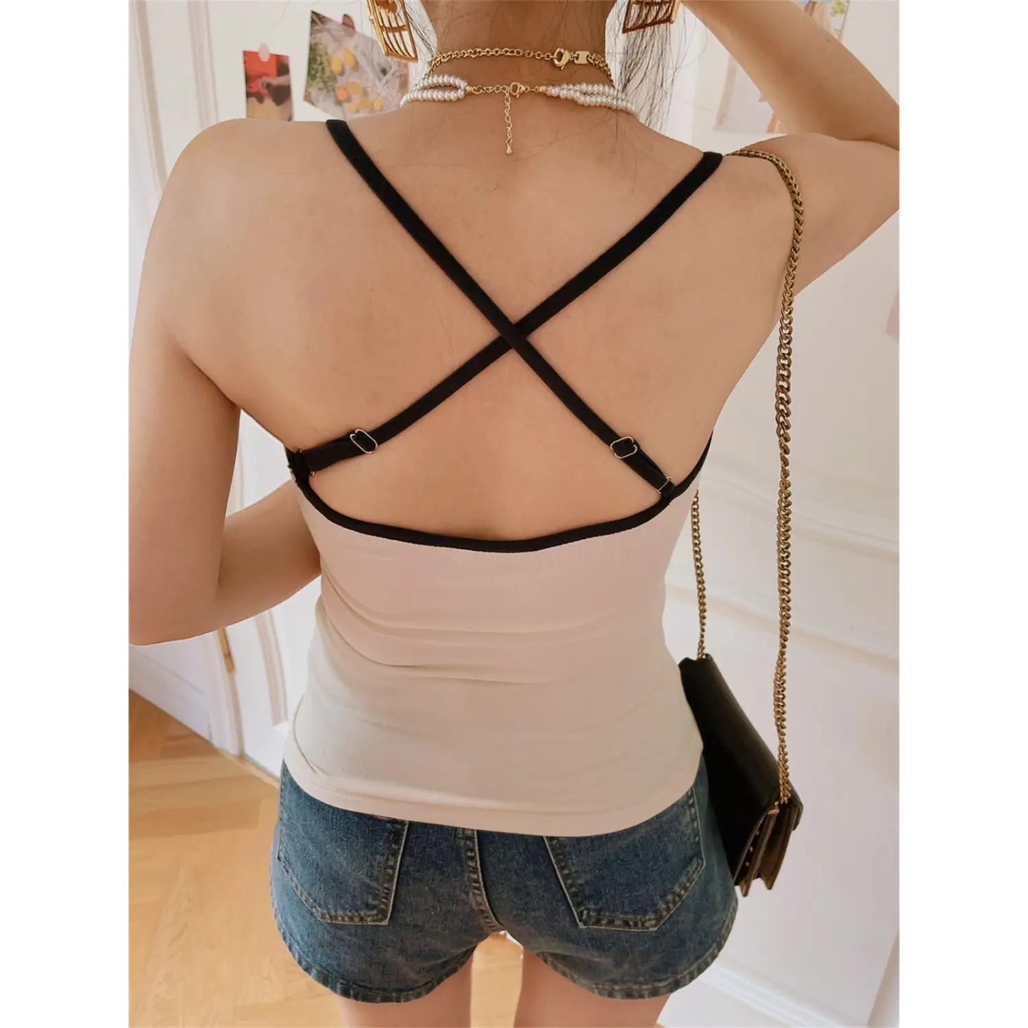Model back view, beige camisole with adjustable black crisscross back straps paired with denim shorts