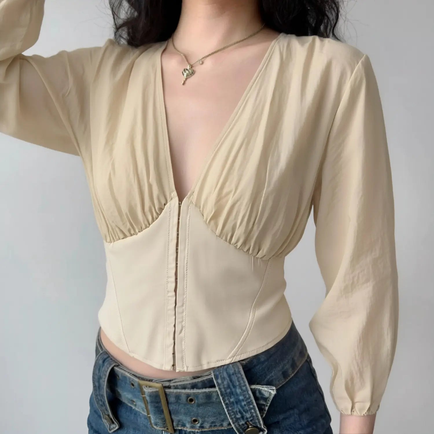 Model wearing beige v‑neck corset crop top, balloon long sleeve, paired with jeans