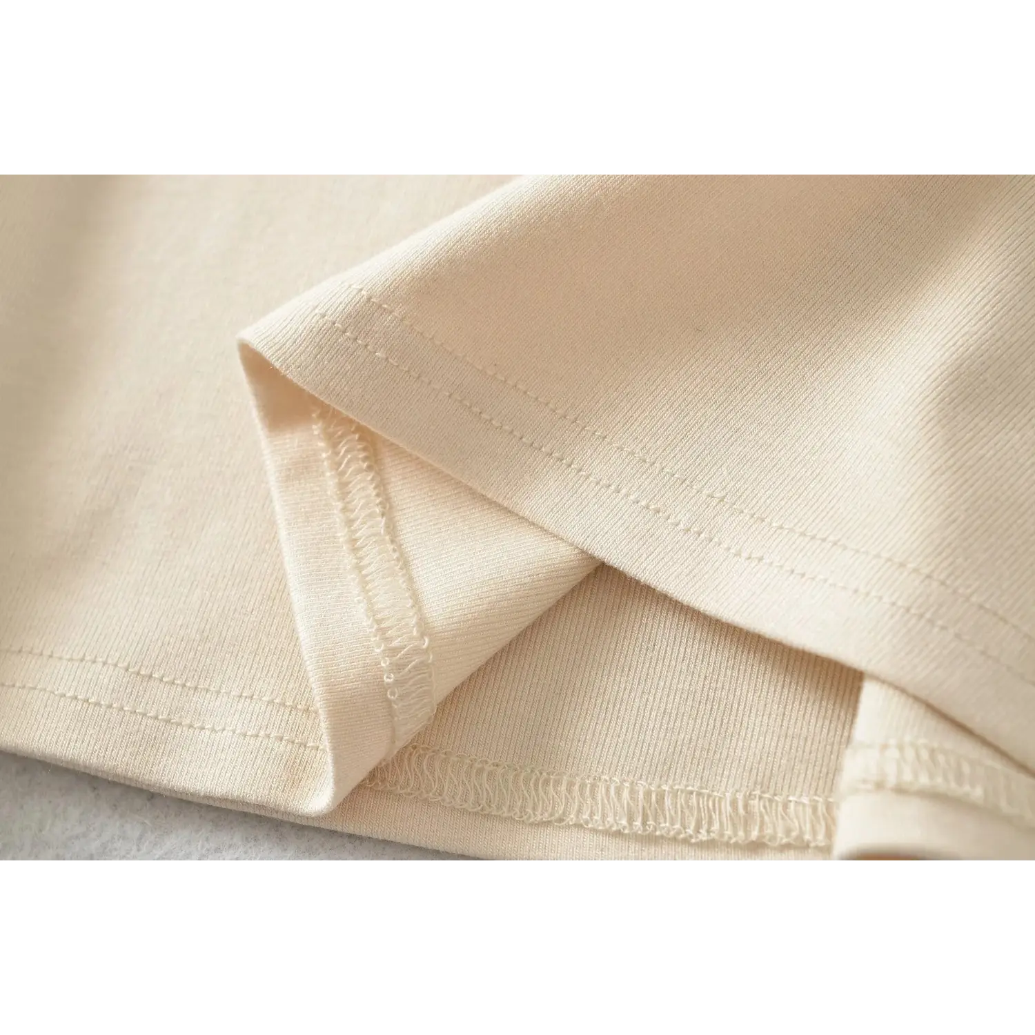 Close up of beige dress fabric and stitching, overlock seam showing soft stretch knit material