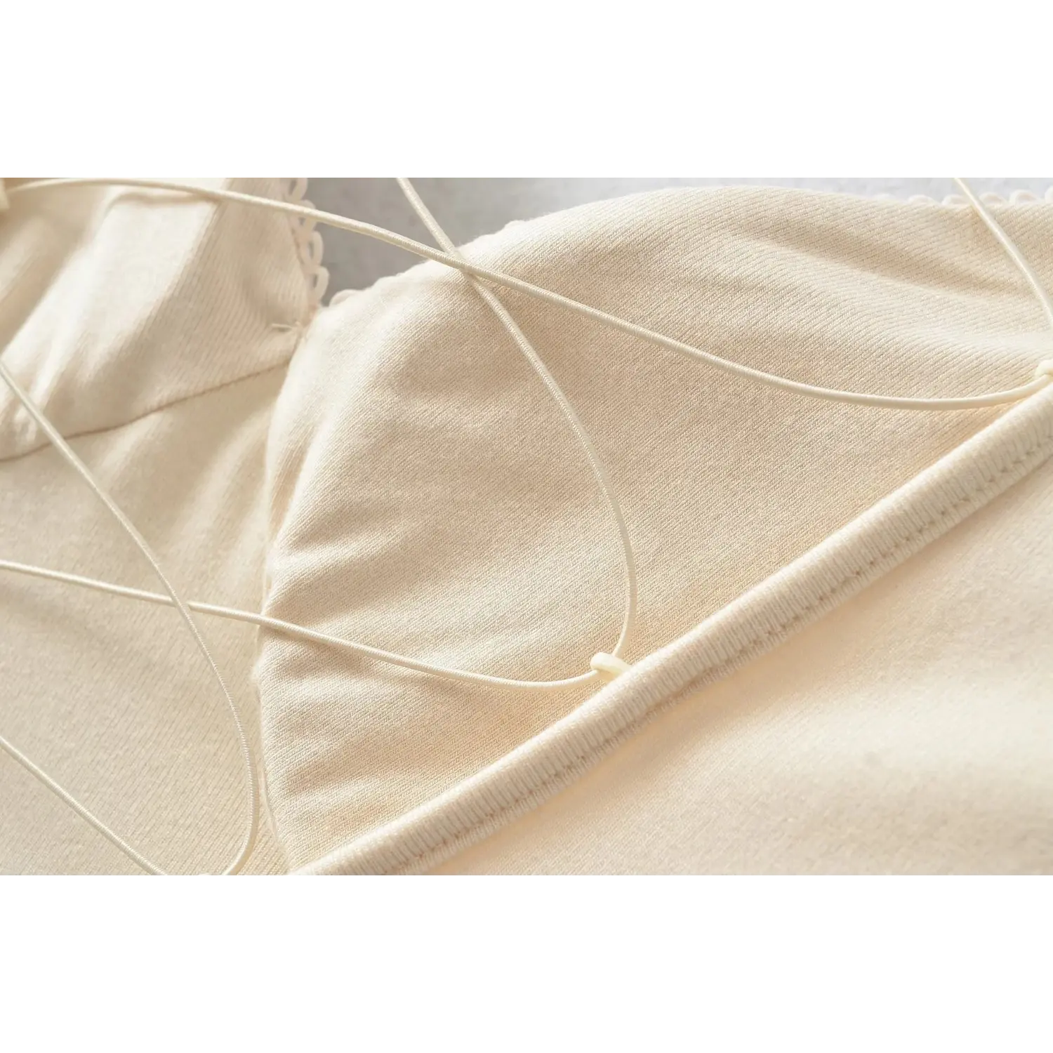 Macro closeup of beige dress crisscross lace straps, soft stretch knit texture and fine stitching detail