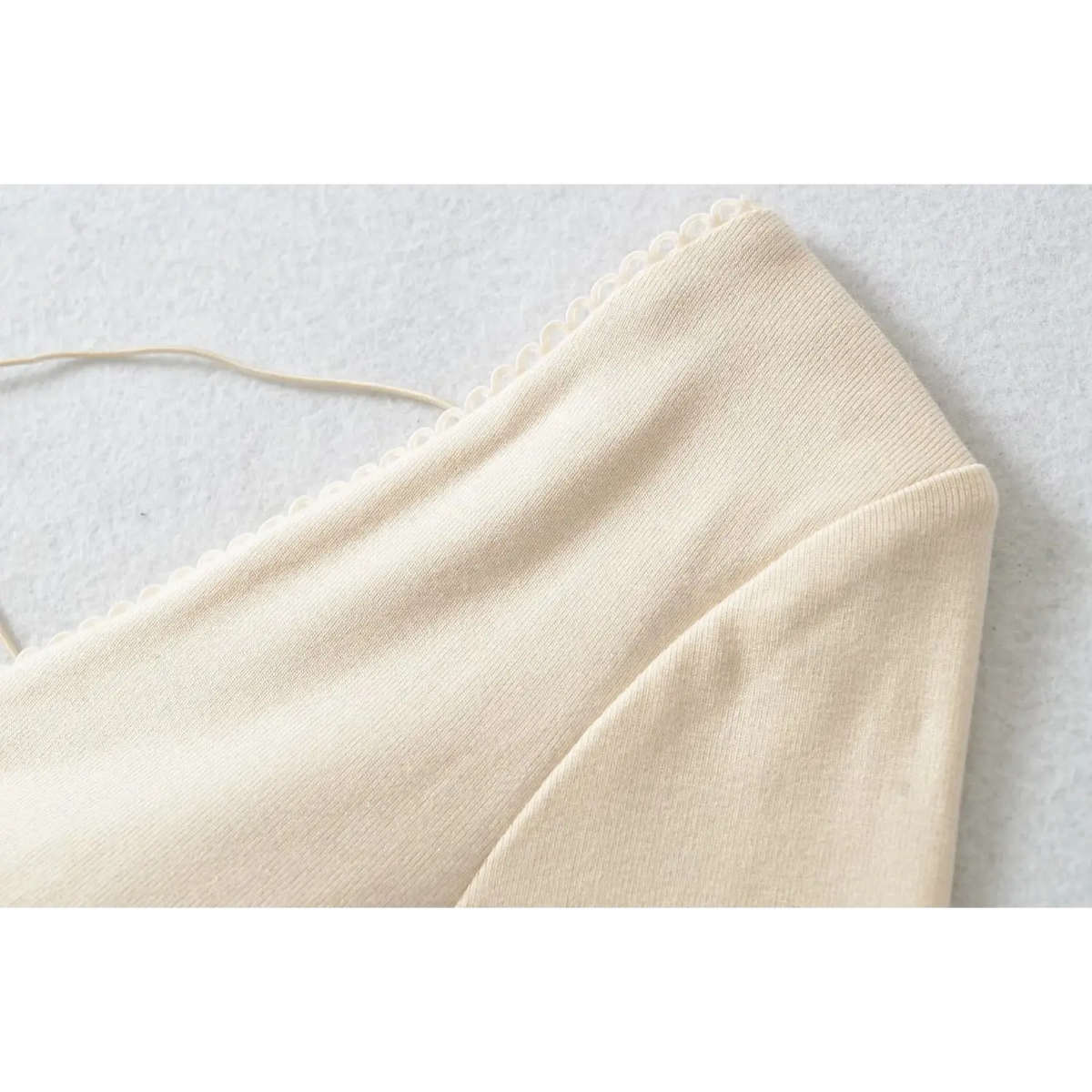 Macro shot of beige dress v neck scalloped lace trim, fine knit texture and crisscross strap detail