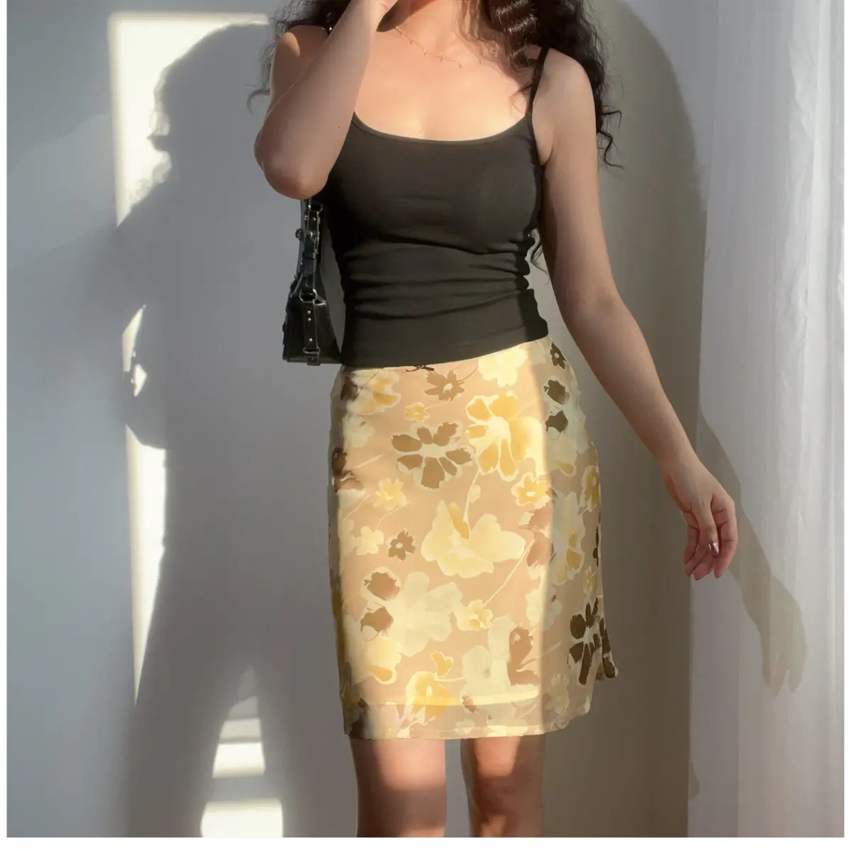 Woman wearing a beige floral chiffon midi skirt with brown and yellow flowers, paired with a black camisole top, showing the skirt's silhouette and print.