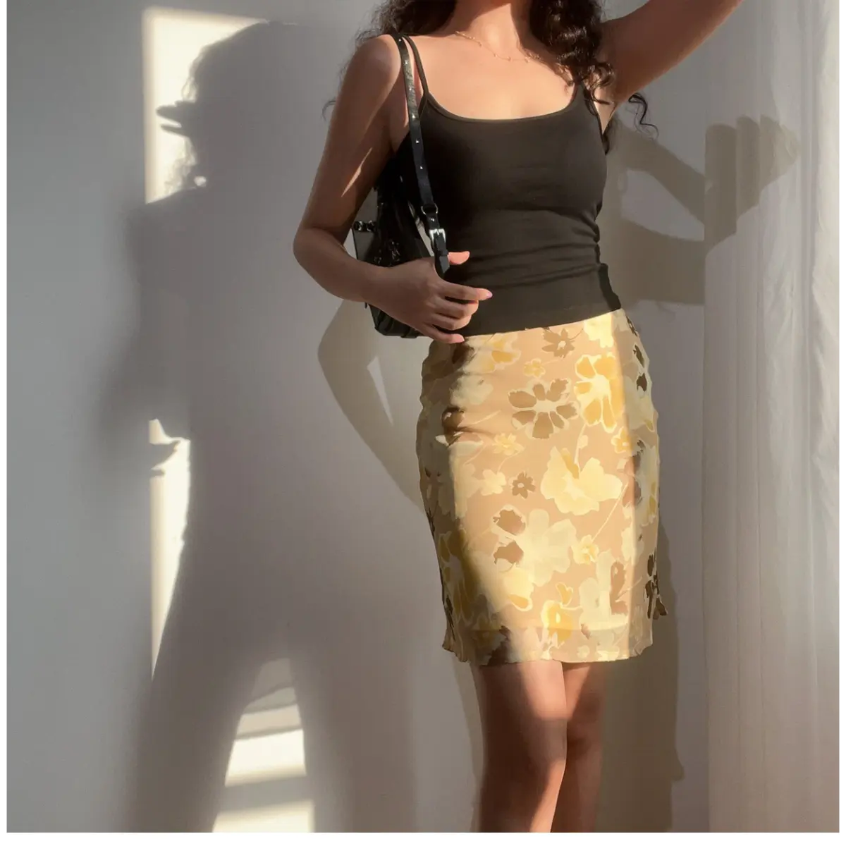 Woman wearing a beige floral chiffon midi skirt with brown and yellow flowers, paired with a black camisole top and carrying a black shoulder bag.