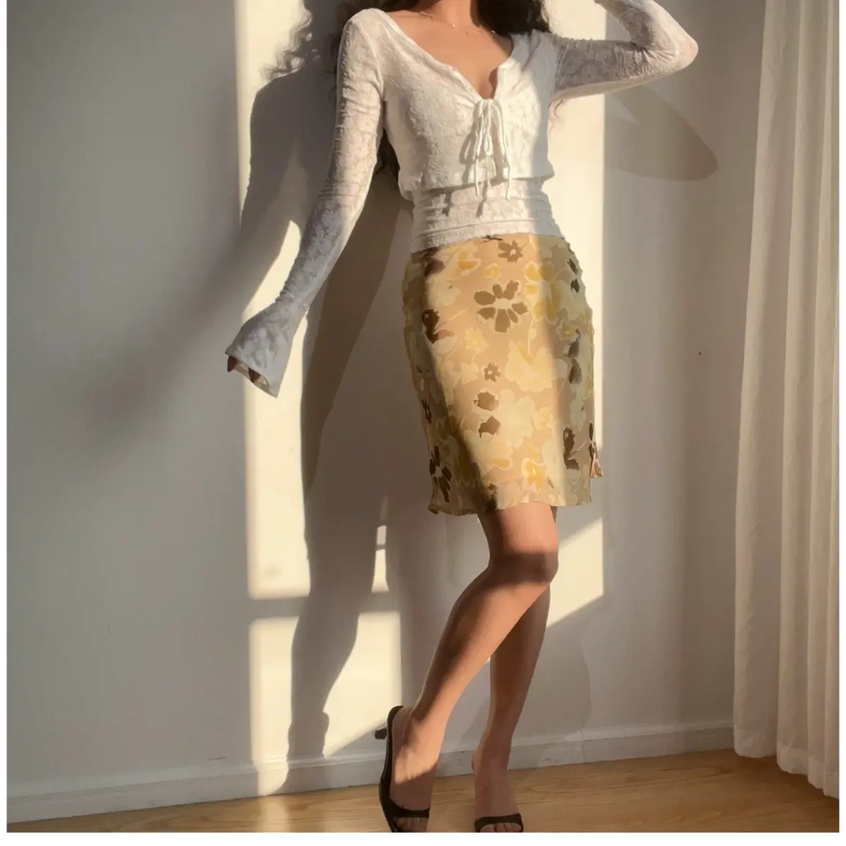 Woman wearing a beige floral chiffon midi skirt with brown and yellow flowers, paired with a white lace long-sleeve cropped top.