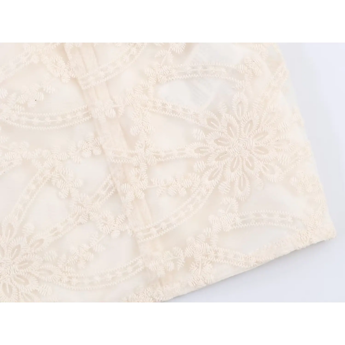 Close-up view of skirt hem and floral embroidery pattern on beige embroidered mini dress, delicate lace texture