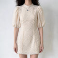 Model wearing beige floral embroidered mini dress, high neck, puff short sleeves, slim fit silhouette, romantic lace design