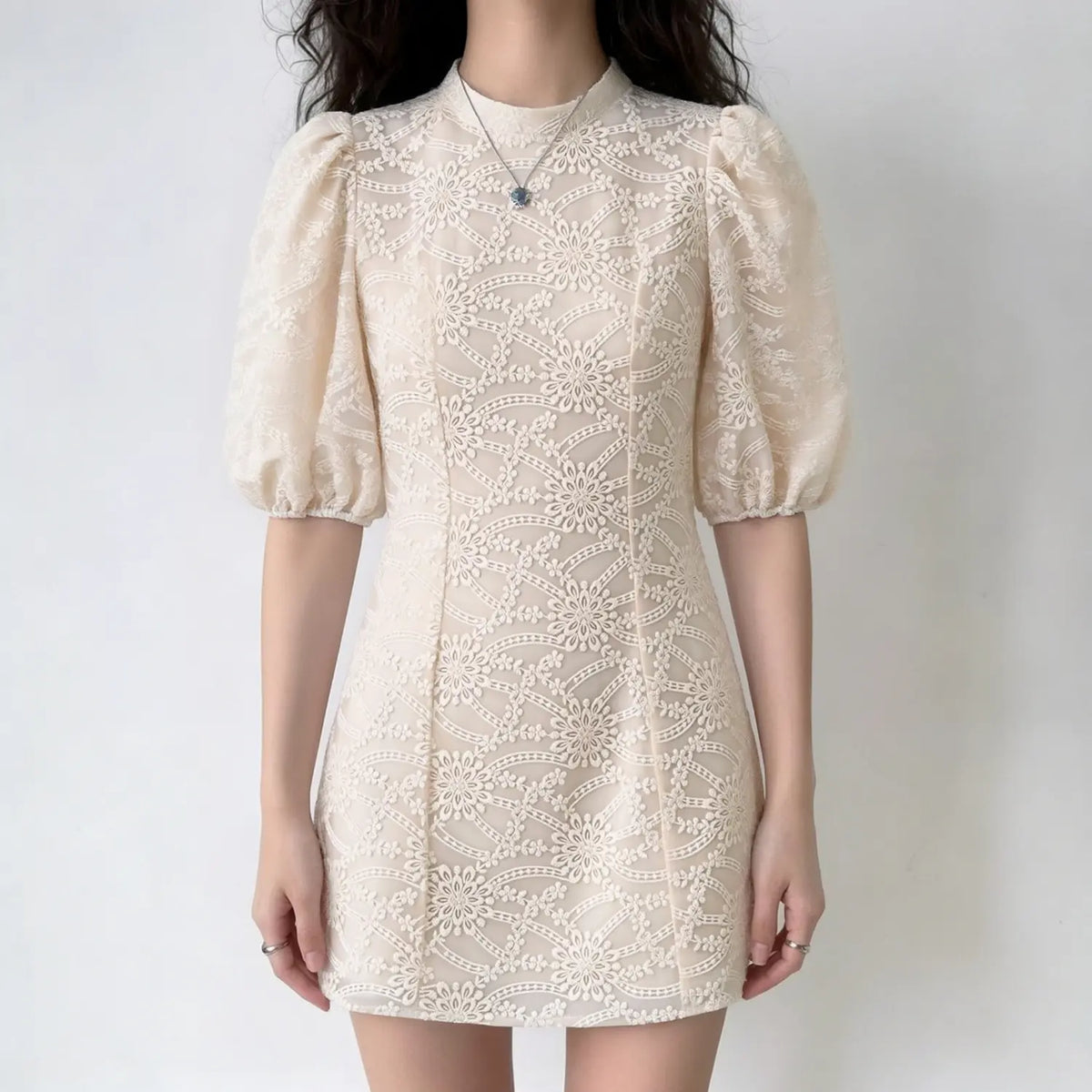 Model wearing beige floral embroidered mini dress, high neck, puff short sleeves, slim fit silhouette, romantic lace design