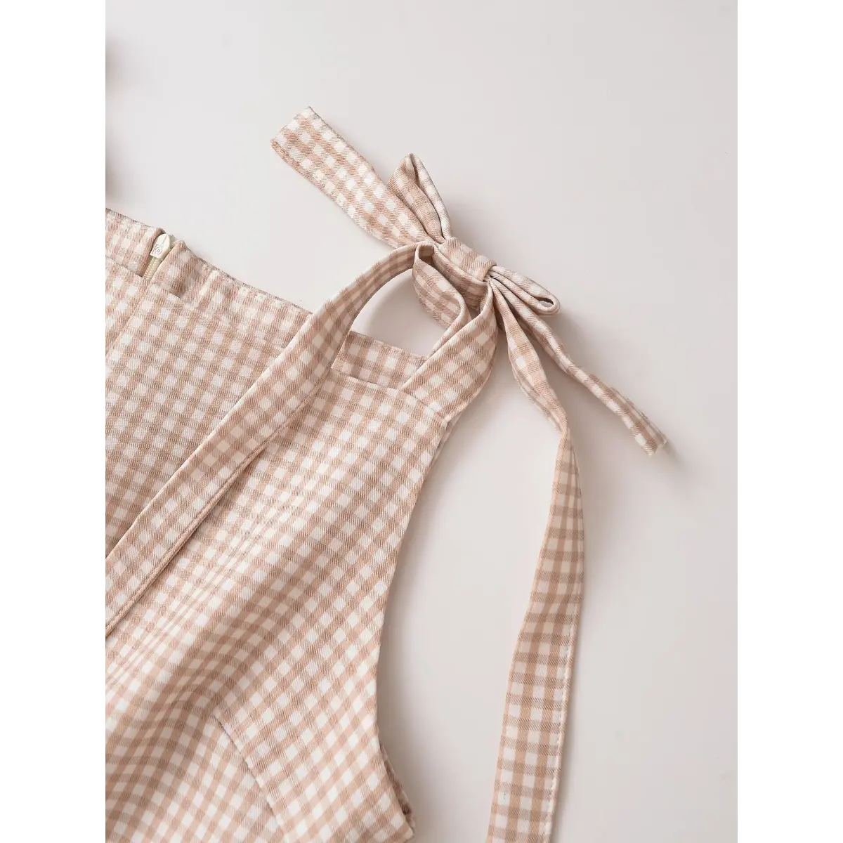 Close-up detail shot of the bow-tied straps on a beige gingham mini dress, showing the back zipper and fabric texture.