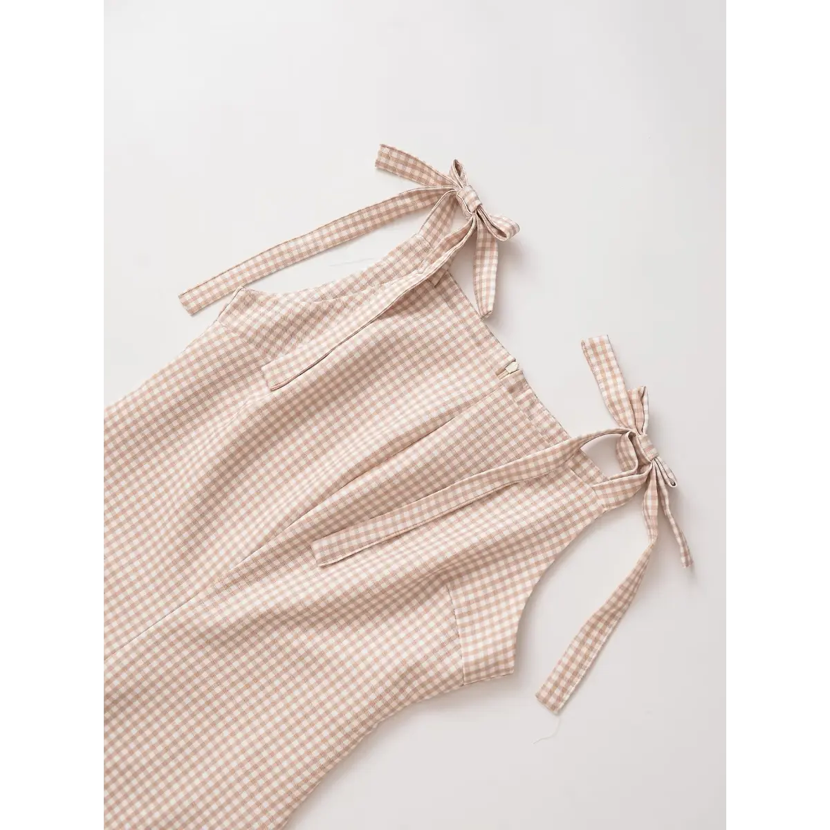 Front view of a beige gingham mini dress with bow-tied straps, showing the fitted bodice and A-line skirt.
