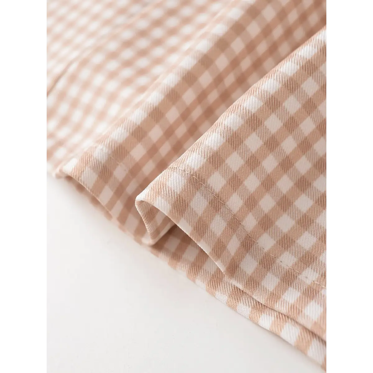 Close-up detail shot of the gingham fabric on a mini dress, showing the weave and hem stitching.