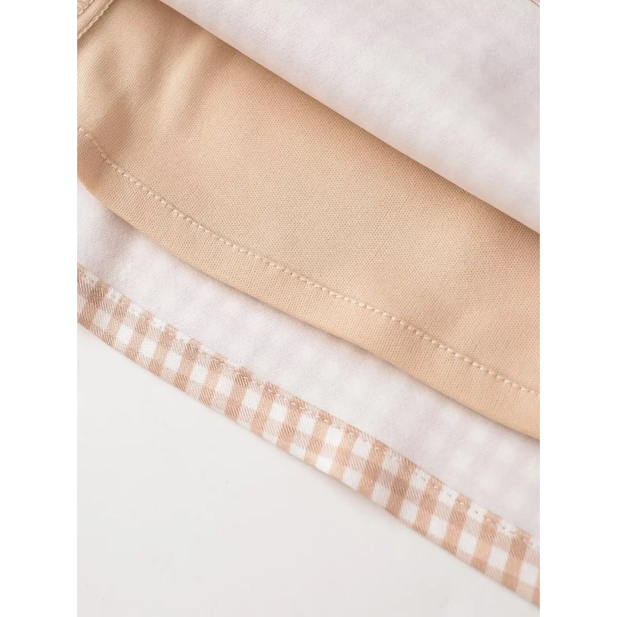 Close-up shot of the inner lining on a beige gingham mini dress, showing the fabric layers and stitching.