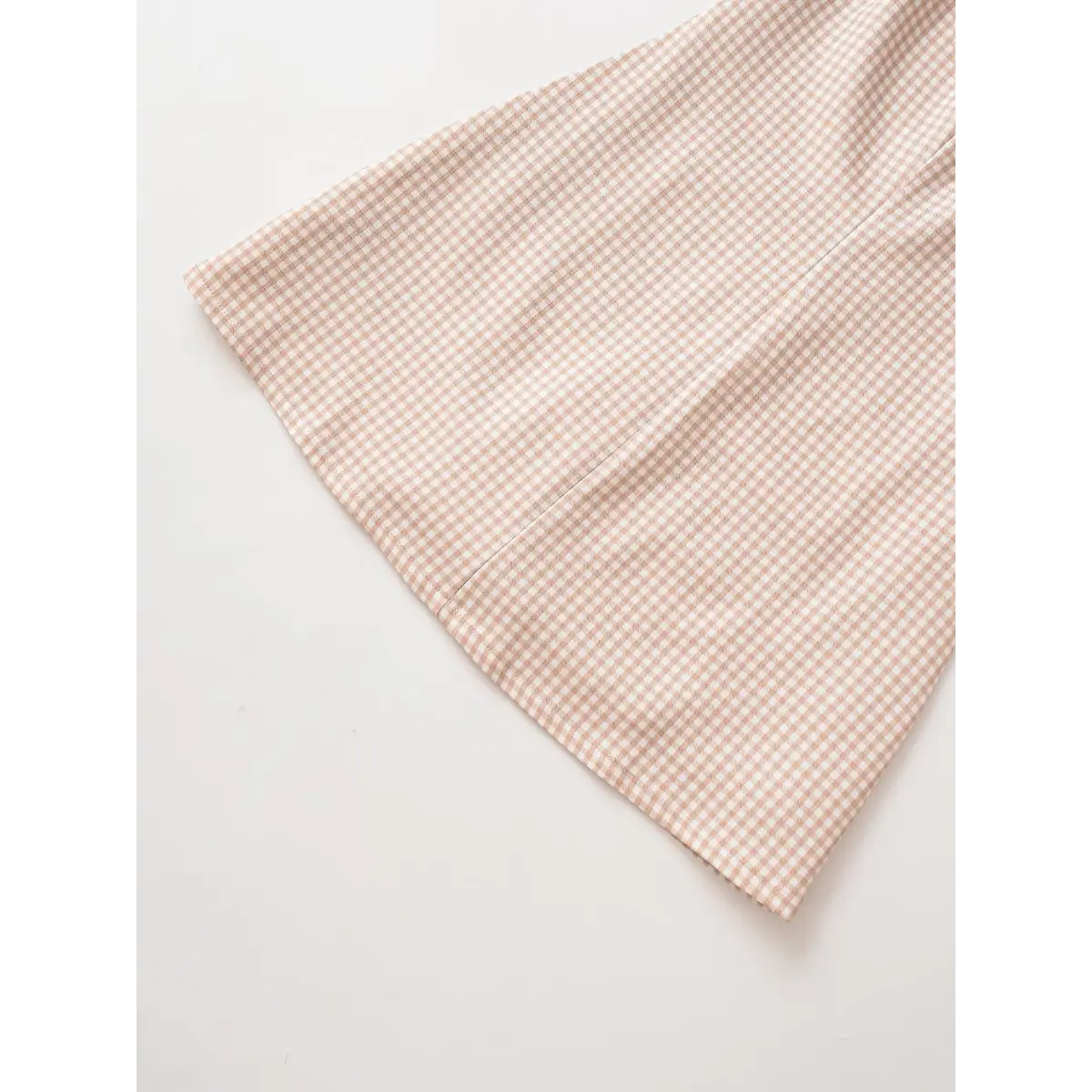 Close-up view of the skirt hem on a beige gingham mini dress, showing the finished edge and fabric pattern.