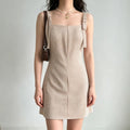 Model wearing a beige gingham mini dress with tie straps, styled with a brown leather bag and pearl necklace, front view.