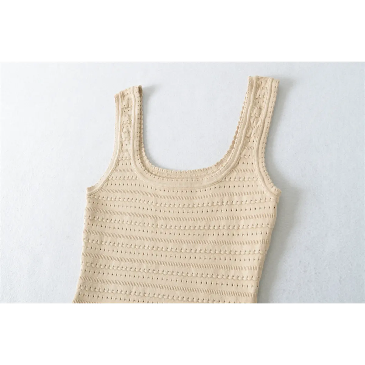 Close-up view of the bodice of a beige knit mini dress, showing the square neckline, wide straps, and openwork pattern.