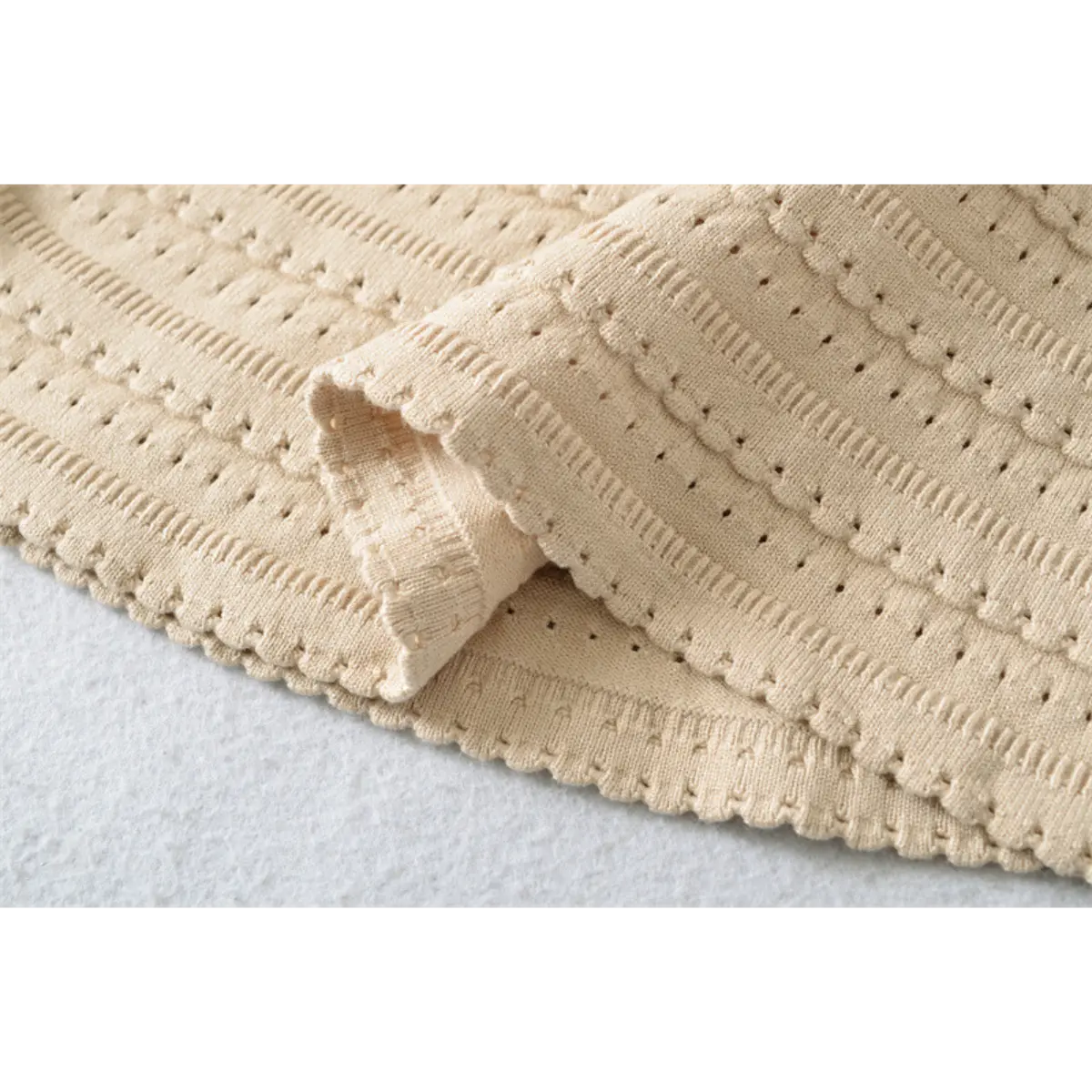 Close-up detail of the textured knit fabric on a beige mini dress, showing the openwork pattern and scalloped hem.