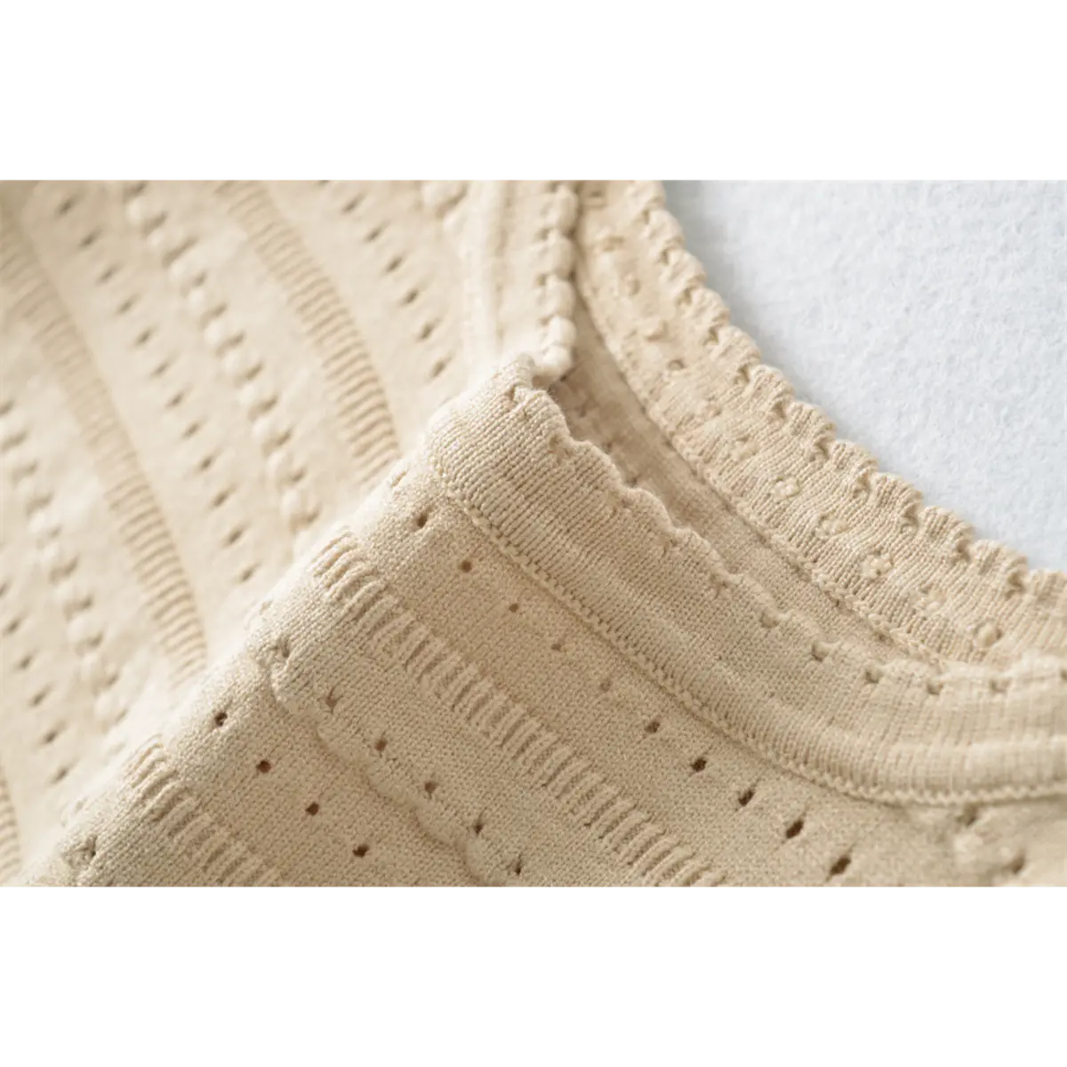 Close-up detail of the square neckline on a beige knit mini dress, showing the scalloped trim and openwork pattern.