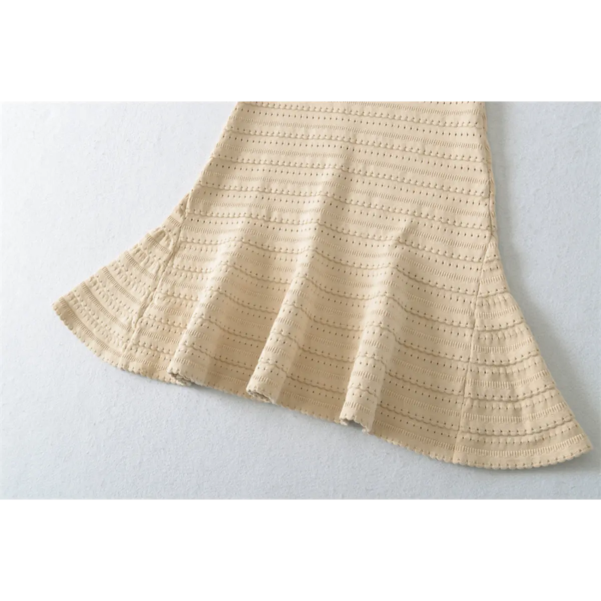 Close-up detail of the flared skirt hem on a beige knit mini dress, showing the openwork pattern and scalloped edge.