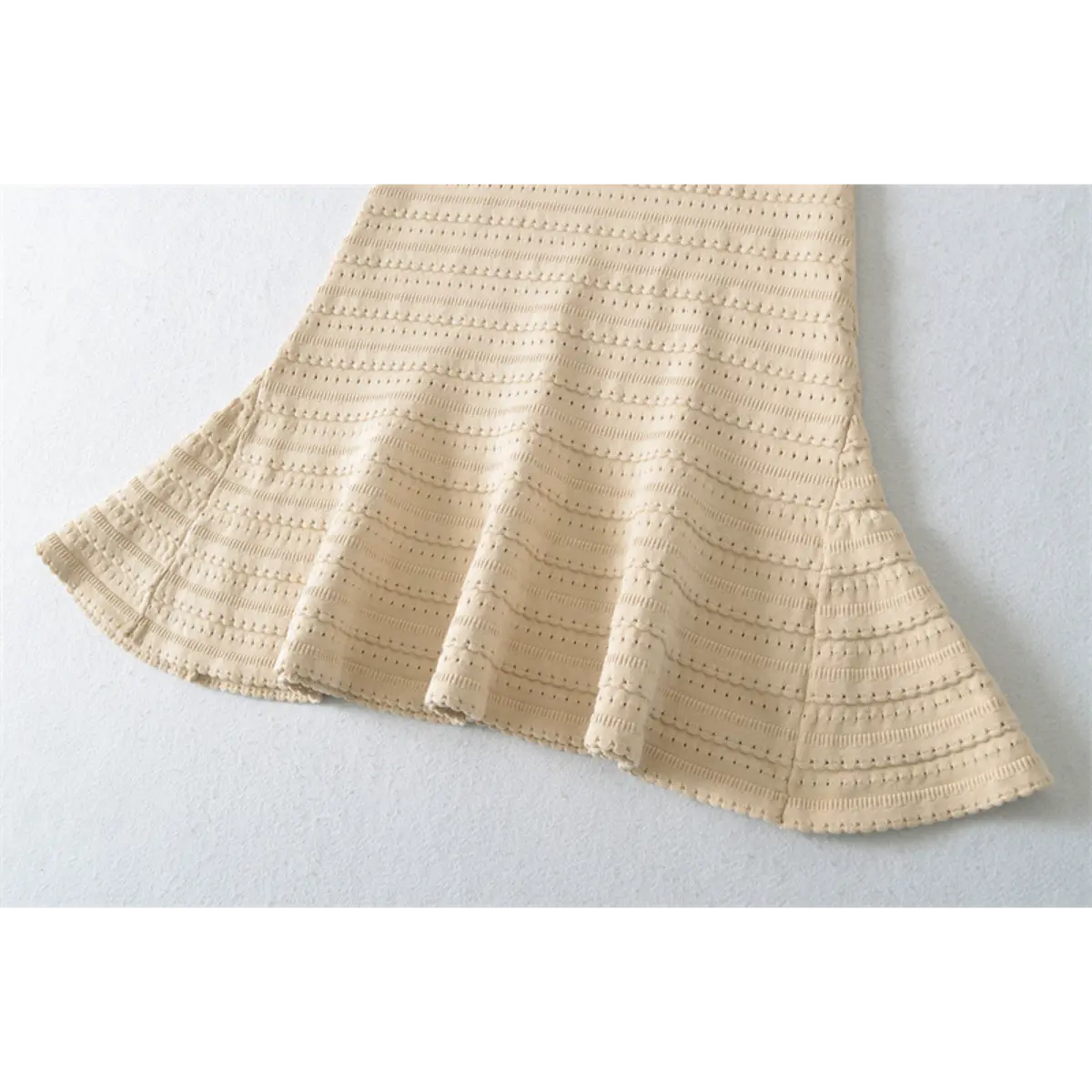 Close-up detail of the flared skirt hem on a beige knit mini dress, showing the openwork pattern and scalloped edge.