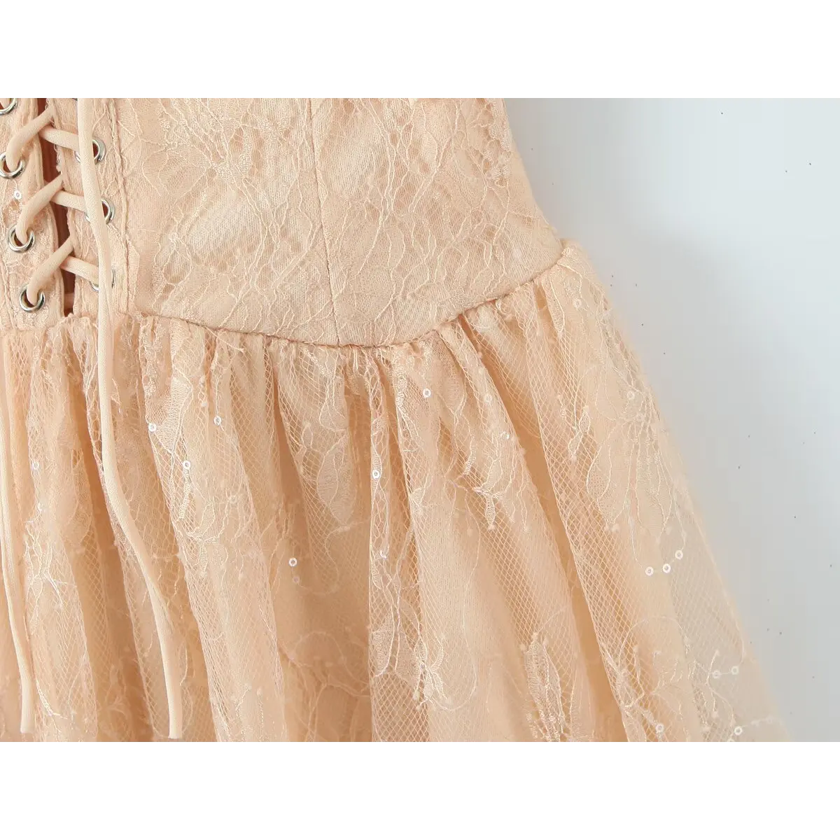 Close-up of the gathered waist seam and lace overlay on the beige cami dress