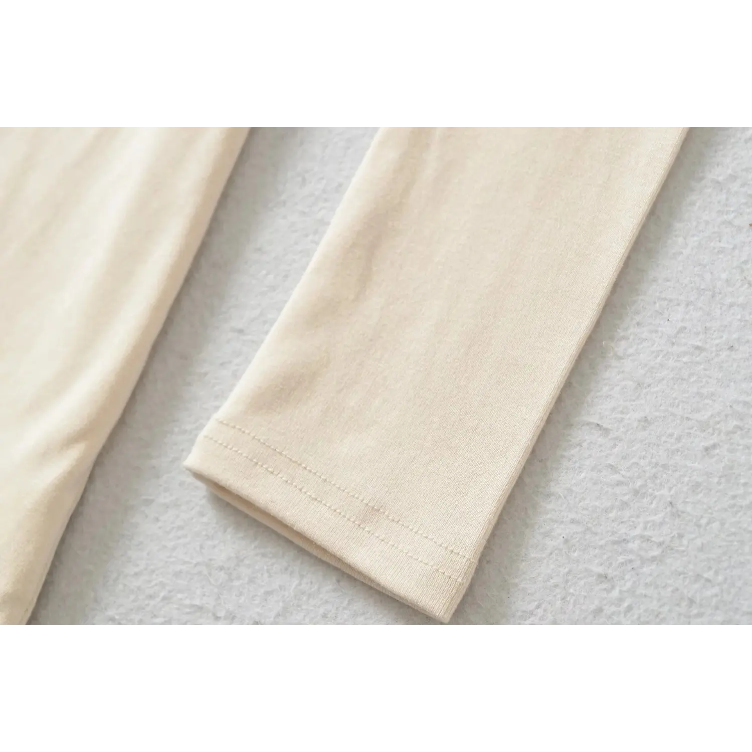 Close up of long sleeve cuff on beige mini dress, neat double stitching, smooth stretch fabric