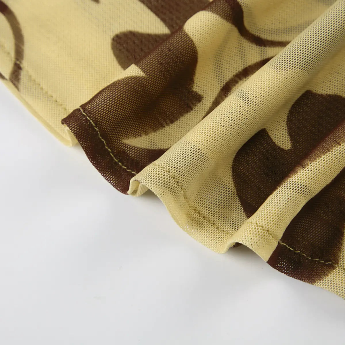 Close-up view of the hem of a beige mesh dress with brown floral print, showing the neat stitching and sheer texture.
