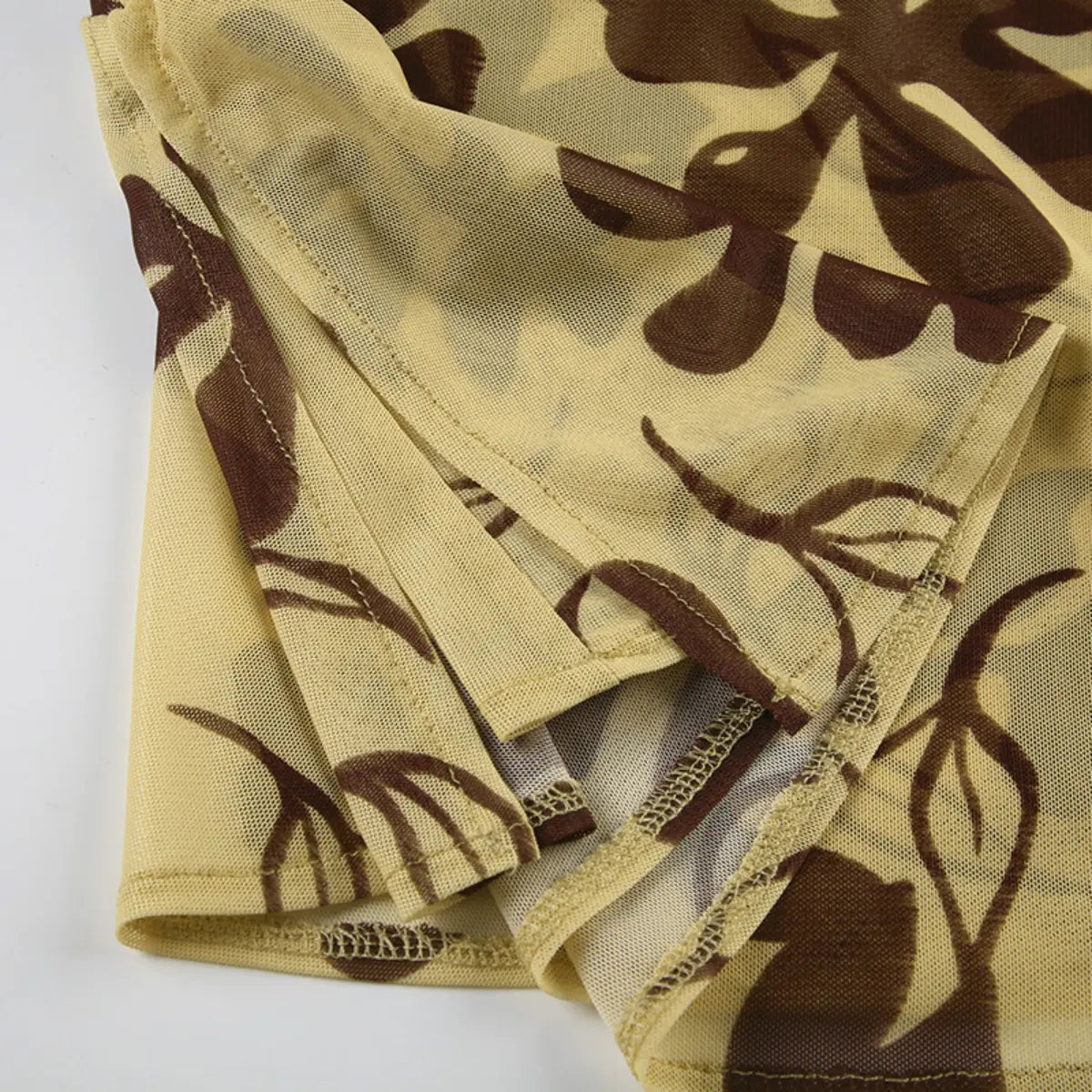 Close-up view of the seams and hem of a beige mesh dress with brown floral print, showing the finishing stitches and sheer texture.
