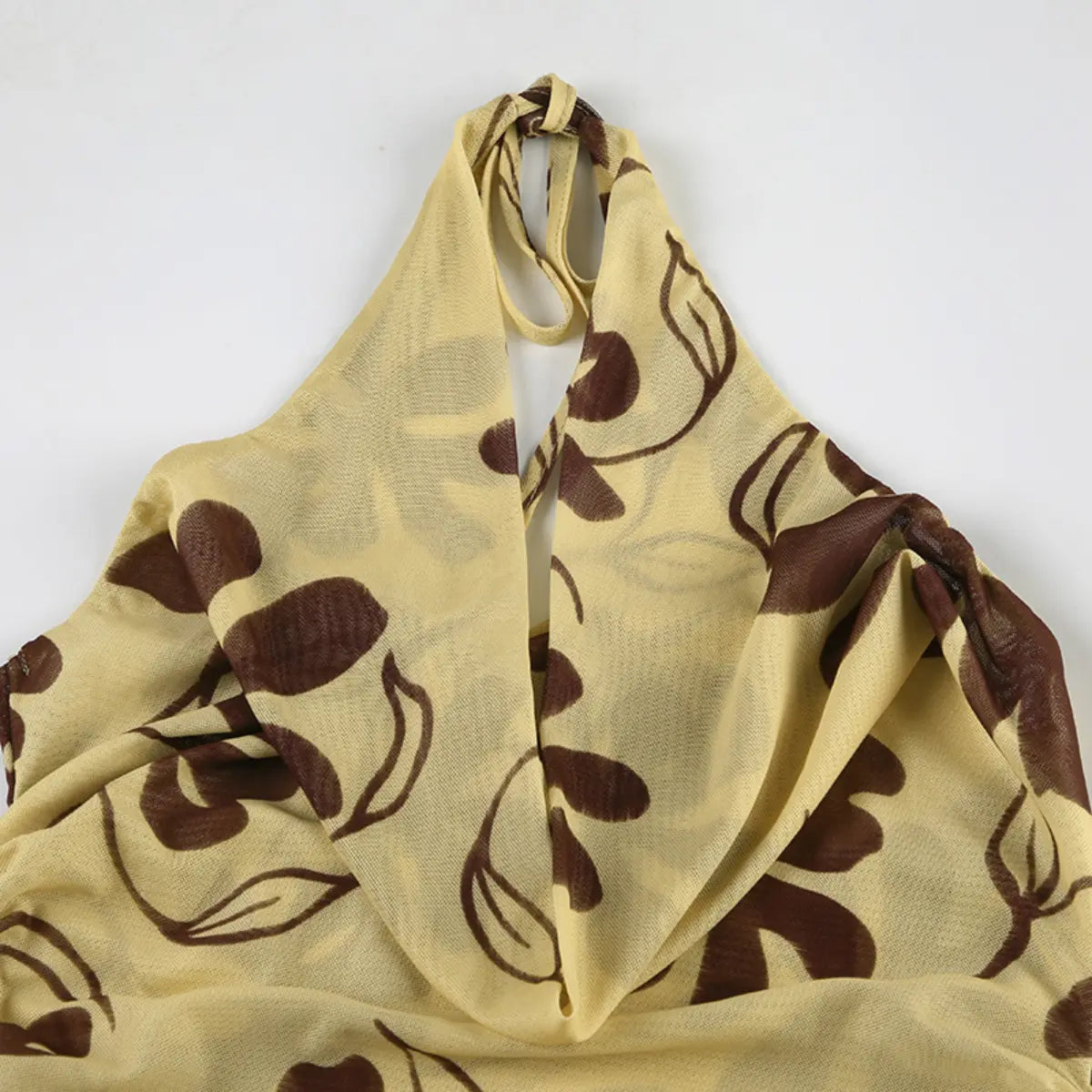 Close-up view of the halter neckline of a beige mesh dress with brown floral print, showing the tie knot, cowl drape, and sheer fabric.