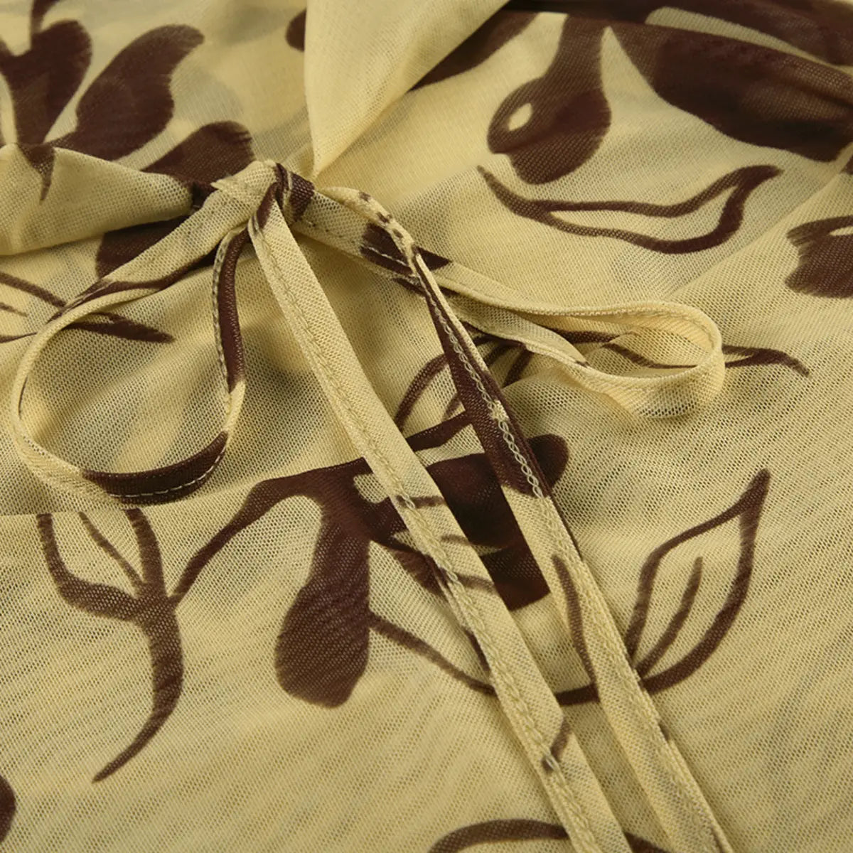 Macro view of the front tie on a beige mesh halter dress with brown floral print, highlighting the stitching and fabric drape.