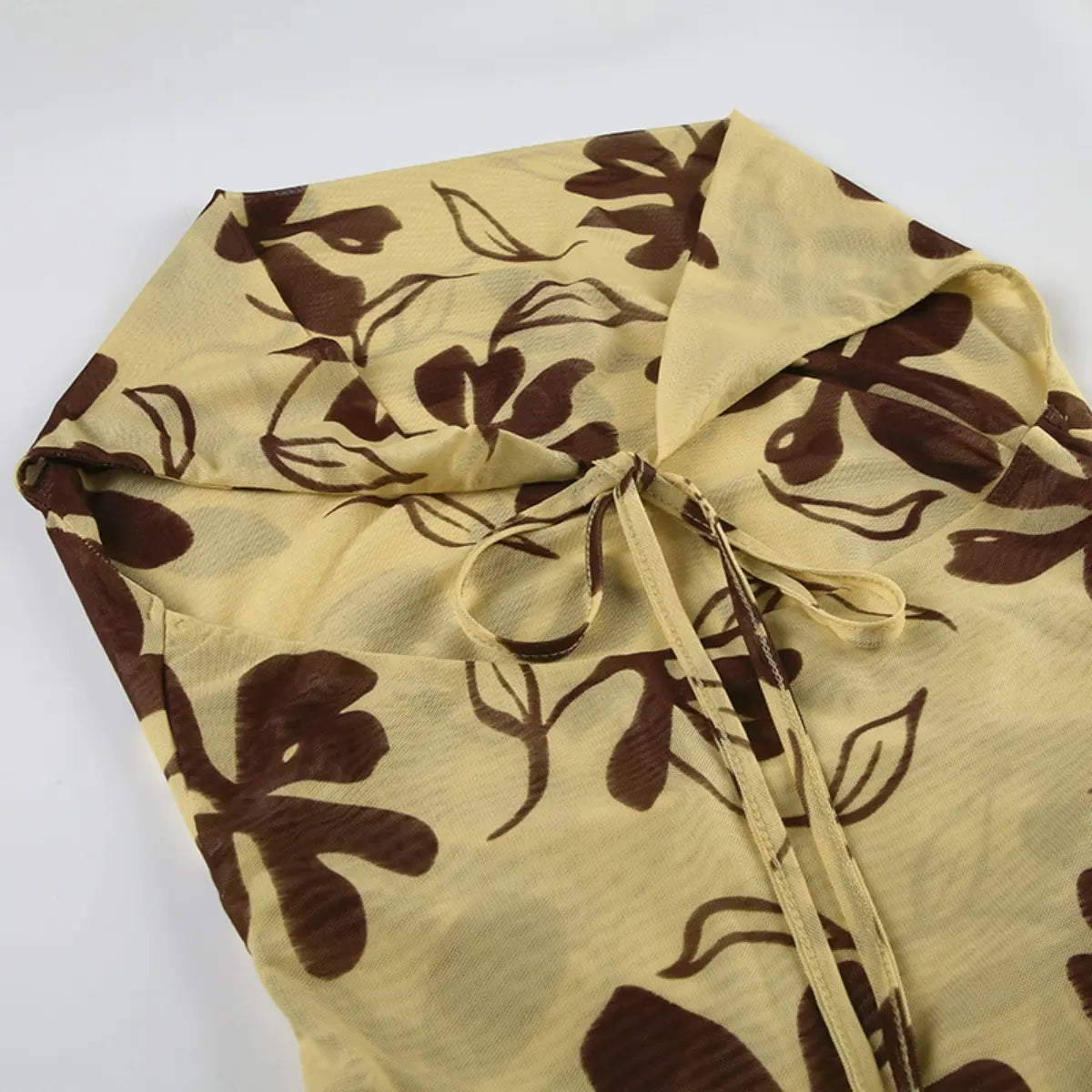 Top-down view of the halter neckline of a beige mesh dress with brown floral print, showing the front tie detail and cowl drape.

