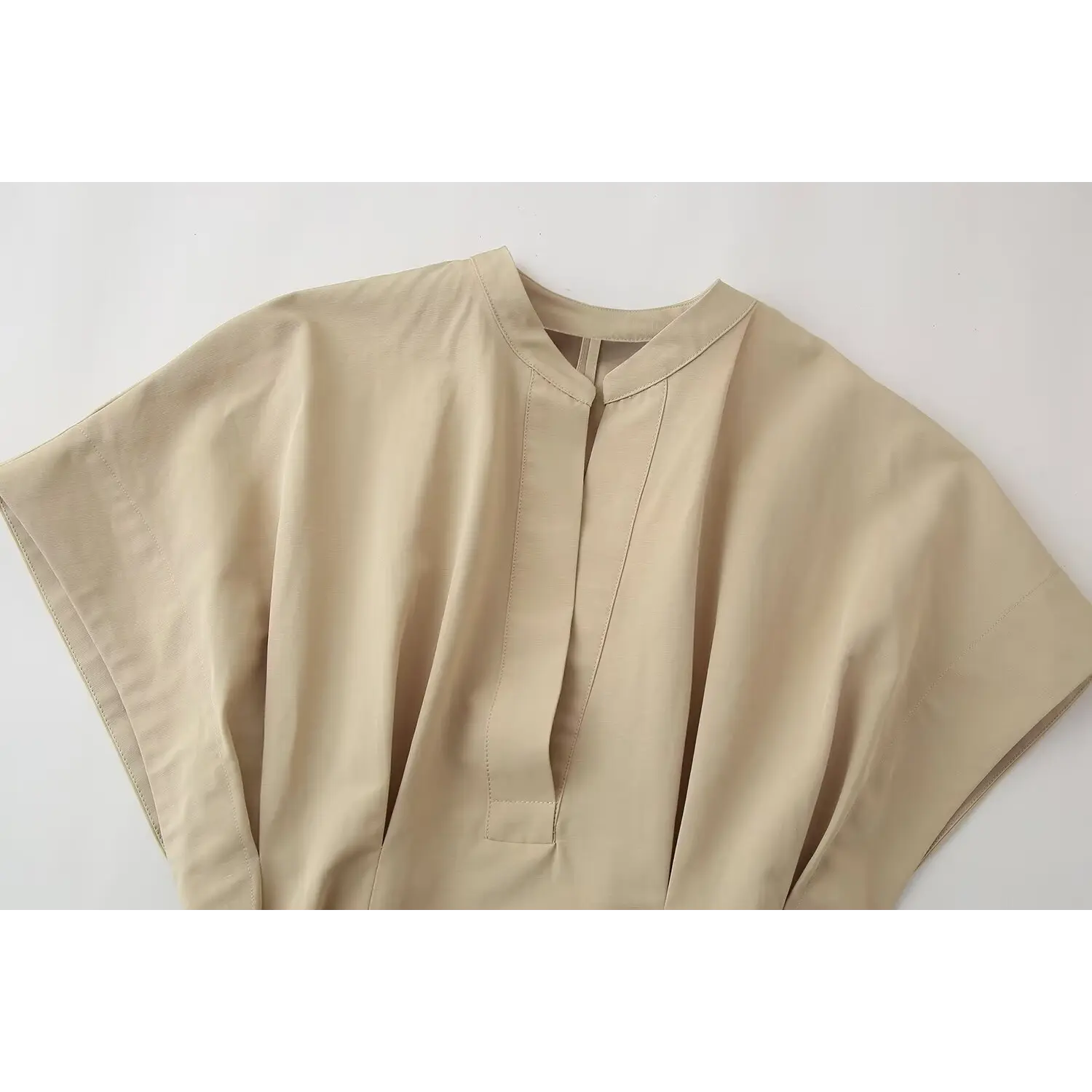 Close‑up of stand collar and half placket stitching detail on beige belted mini dress