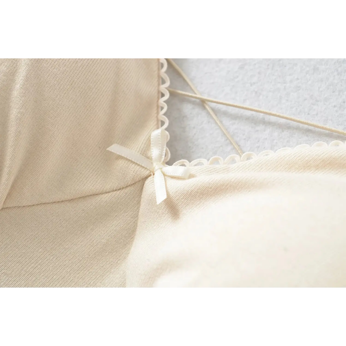 Close up of small white satin bow at bust of beige long sleeve mini dress, scalloped neck edge