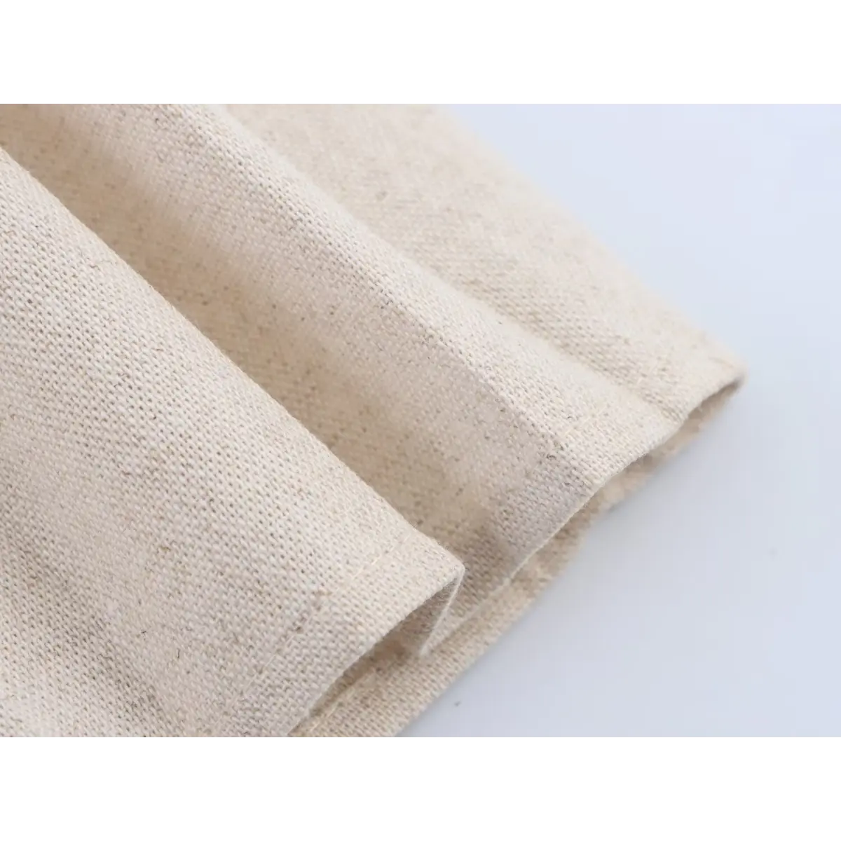 Close-up shot of the beige woven fabric on the pleated skirt of a black faux-leather mini dress, showing the texture and stitching.