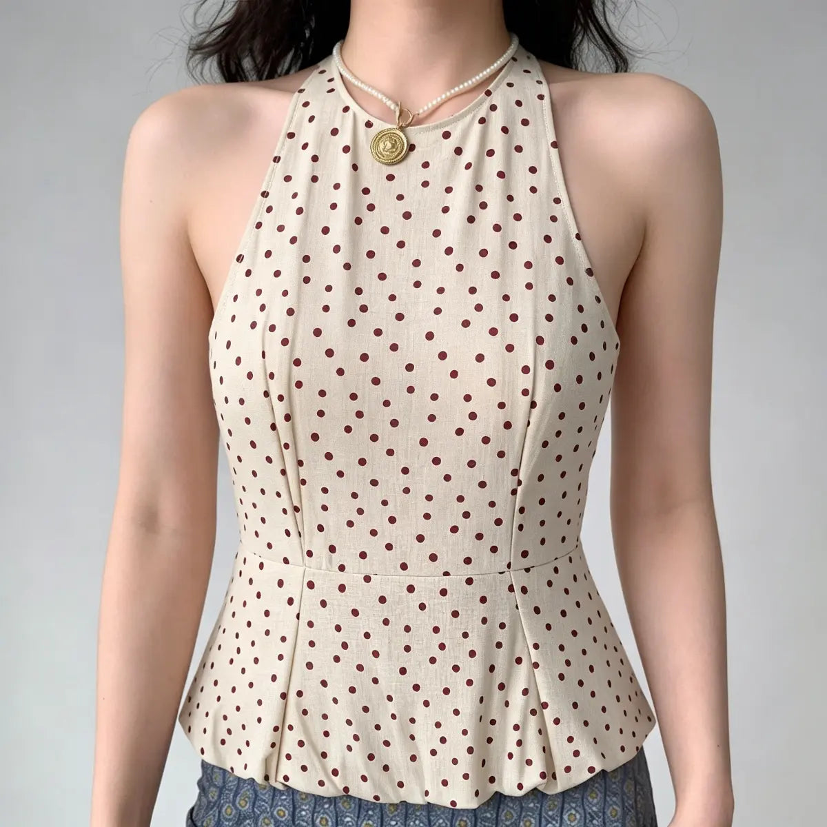 Front view of a beige halter peplum top with red polka dots, highlighting the tailored construction, princess seams, and flared peplum hem.