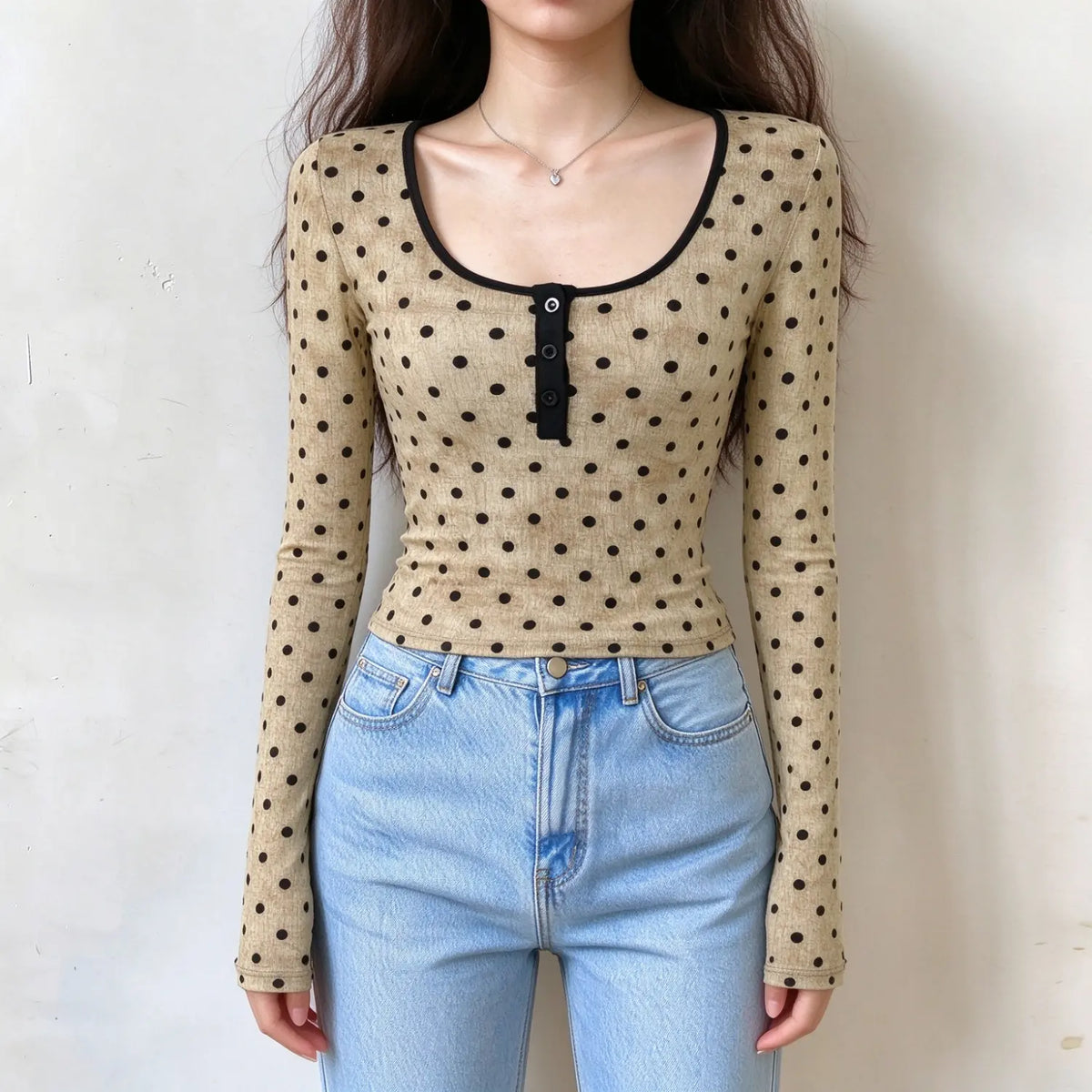 Model wearing beige polka dot long sleeve fitted top, scoop neck with black trim, henley button placket, slim cropped fit, paired with light blue jeans on plain white wall