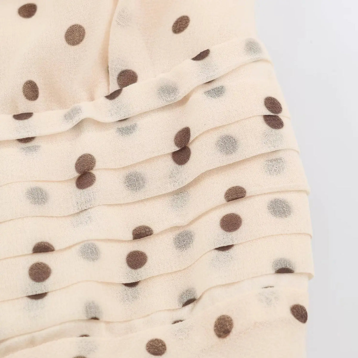 Close‑up of sheer hem edge and brown polka dot pattern on beige maxi dress