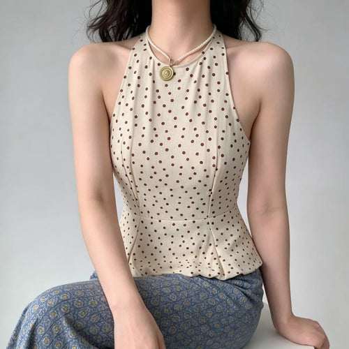 Model wearing a beige halter peplum top with red polka dots, featuring a high neck, fitted bodice, and flared peplum hem, styled with blue floral pants.