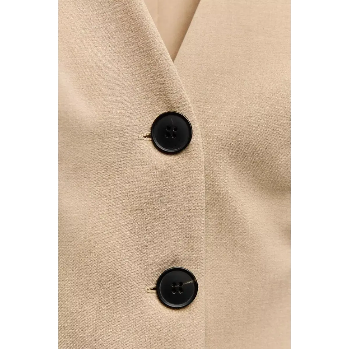  Close-up of black four-hole button detailing on the beige tailored vest-style pleated mini dress, highlighting precise stitching.