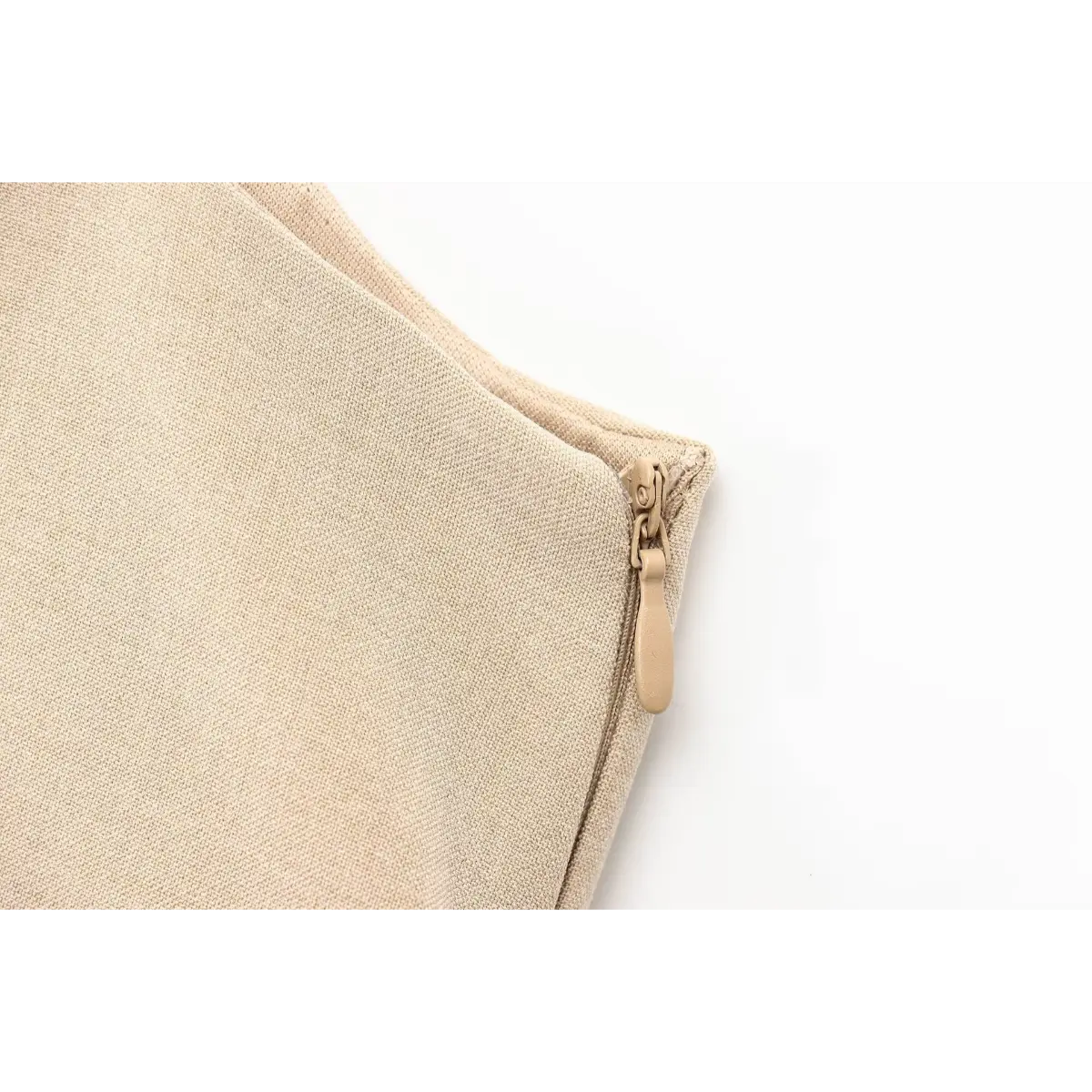 Close-up of the hidden side zipper on the beige pleated mini dress, featuring a matching fabric pull tab.