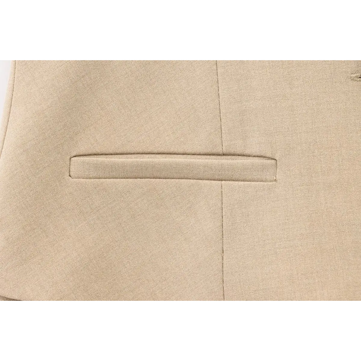Close-up of the clean welt pocket on the beige tailored vest dress, showing sharp, tailored construction.