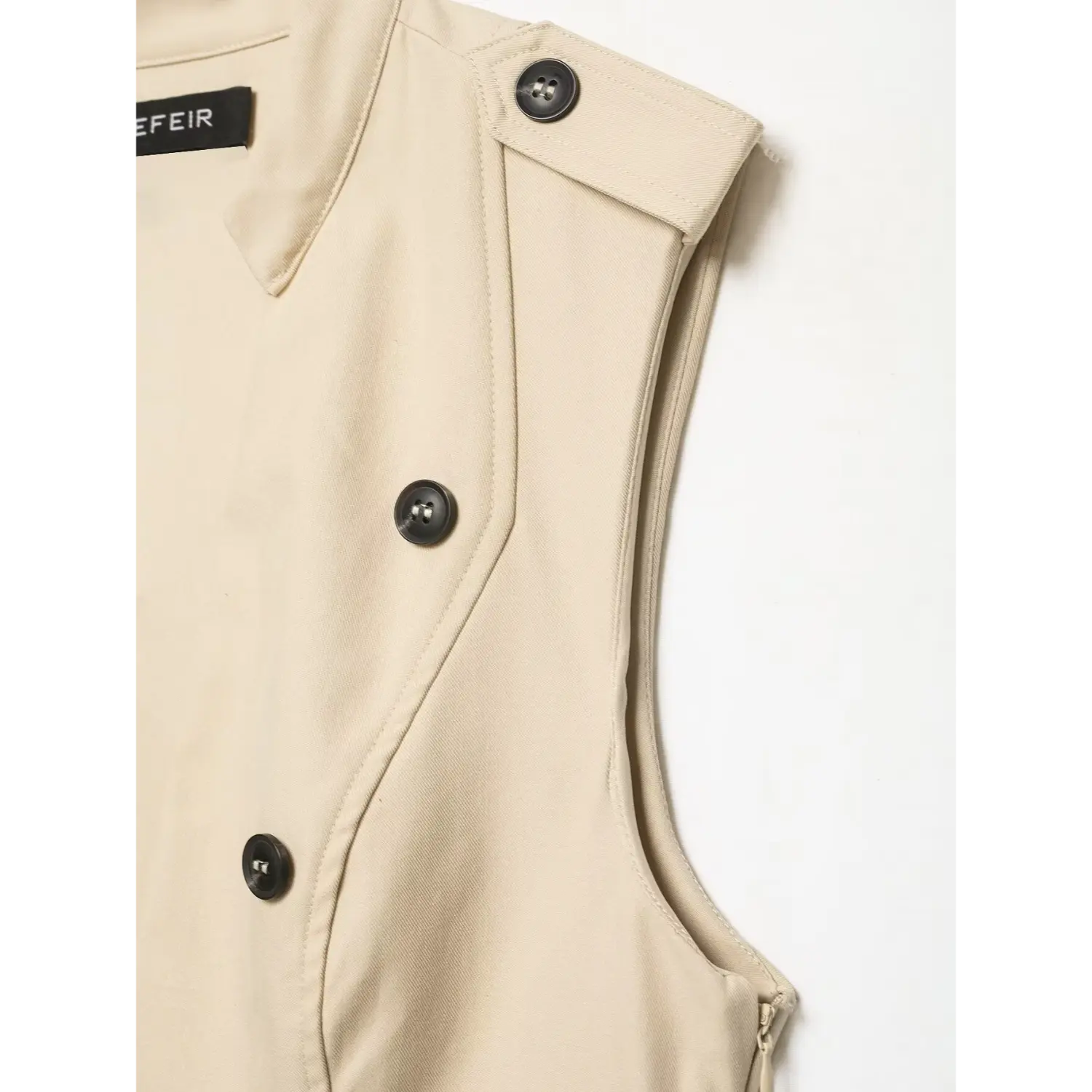 Close‑up of shoulder epaulet, armhole stitching and black buttons on beige sleeveless trench dress