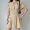 Model wearing beige v‑neck short sleeve mini dress with matching waist belt, pleated skirt, casual elegant women outfit, grey background