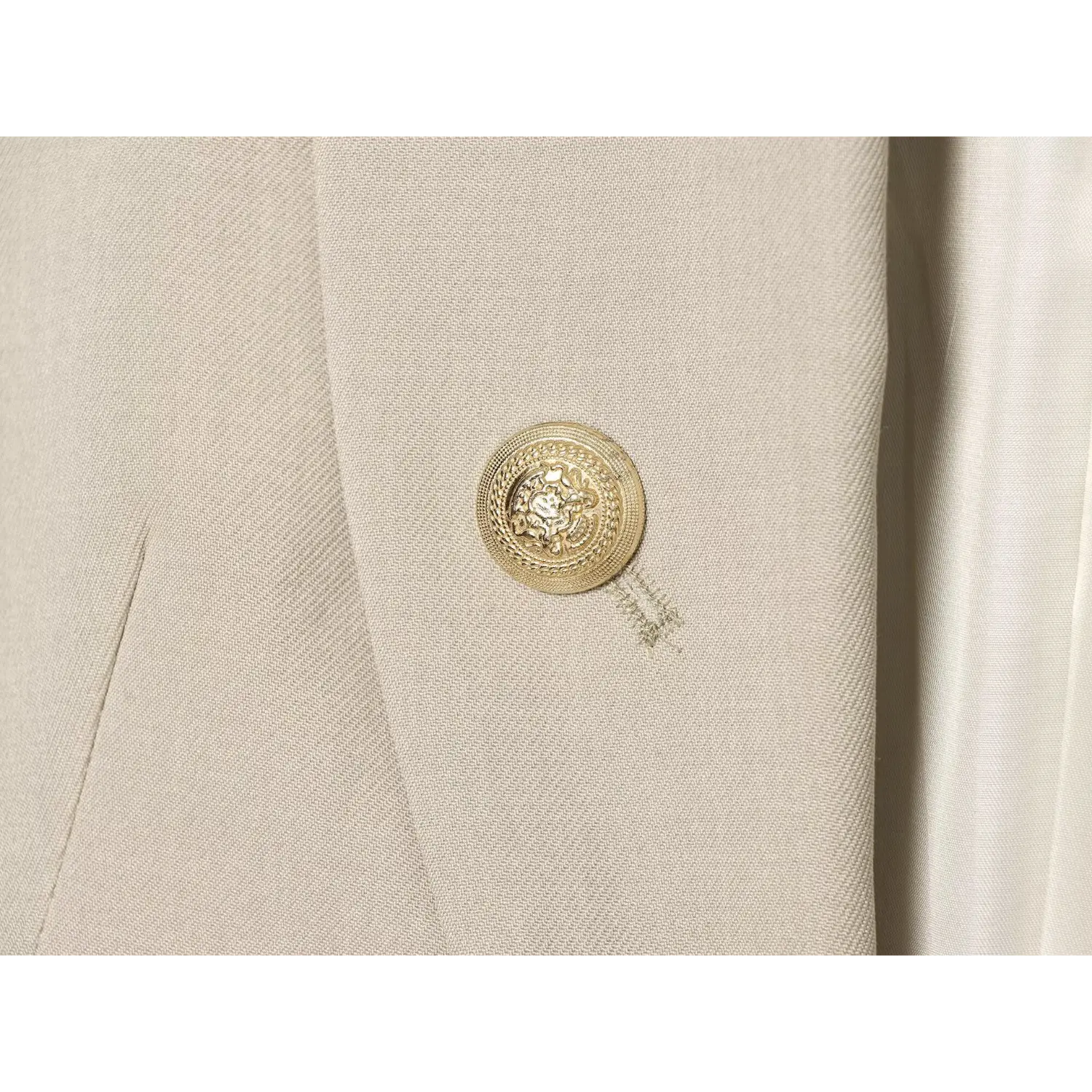 Macro close‑up of ornate embossed gold metal button on beige vest